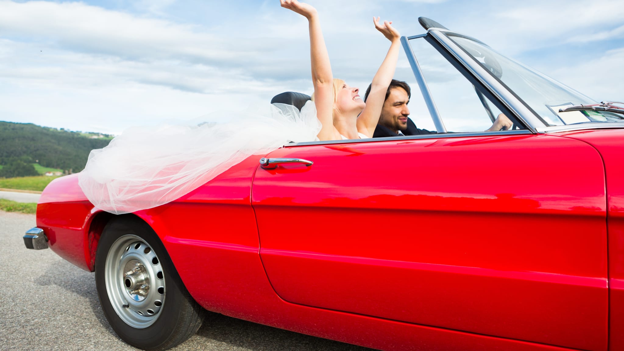 Ein Hochzeitspaar in einem roten Cabrio.
