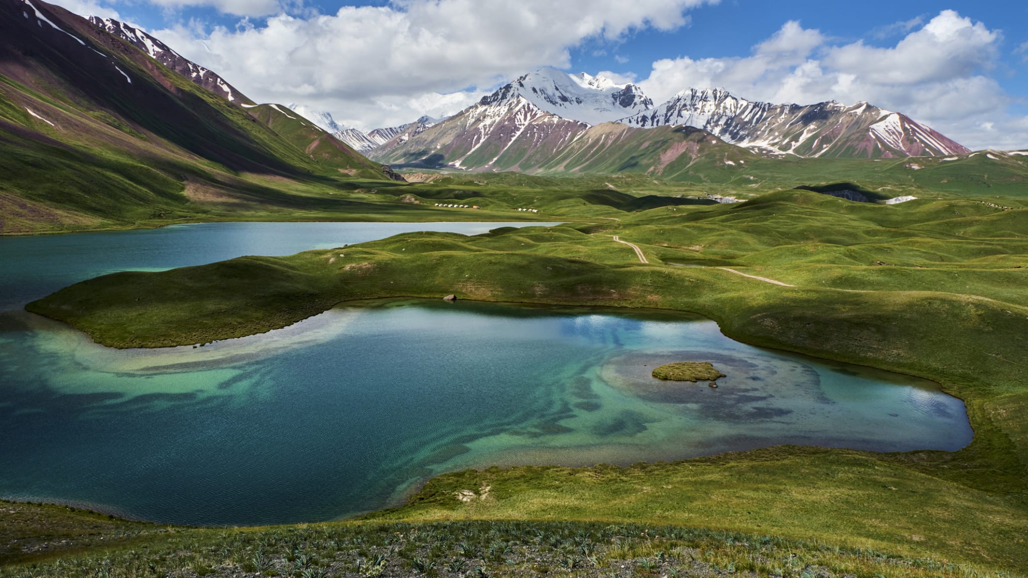Ein See mit grünen Hügeln und einem Gebirge im Hintergrund, Kirgistan.