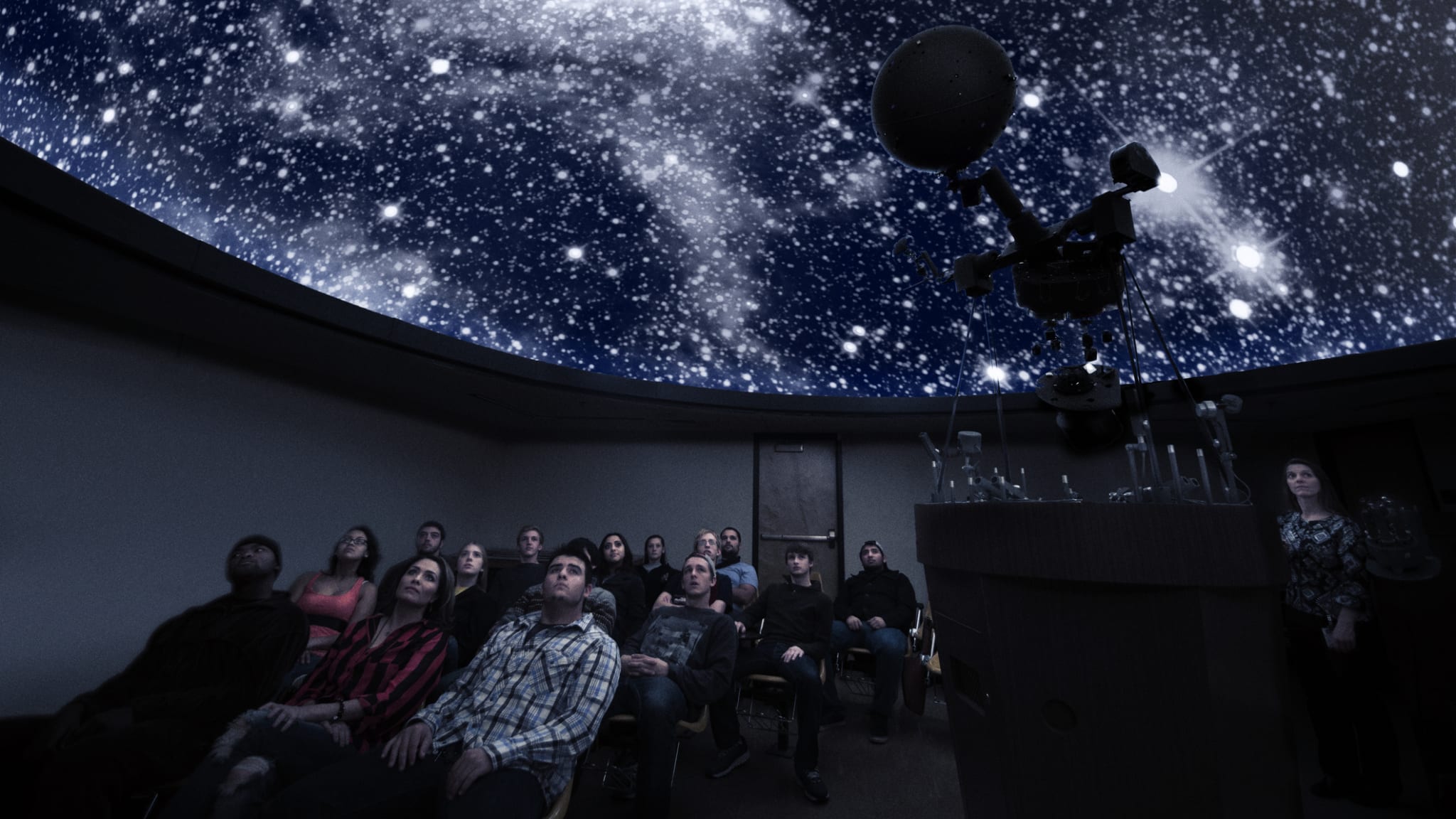 Eine Gruppe von Menschen sitzt in einem Planetarium und lauscht der Vorstellung. © Hill Street Studios/DigitalVision via Getty Images