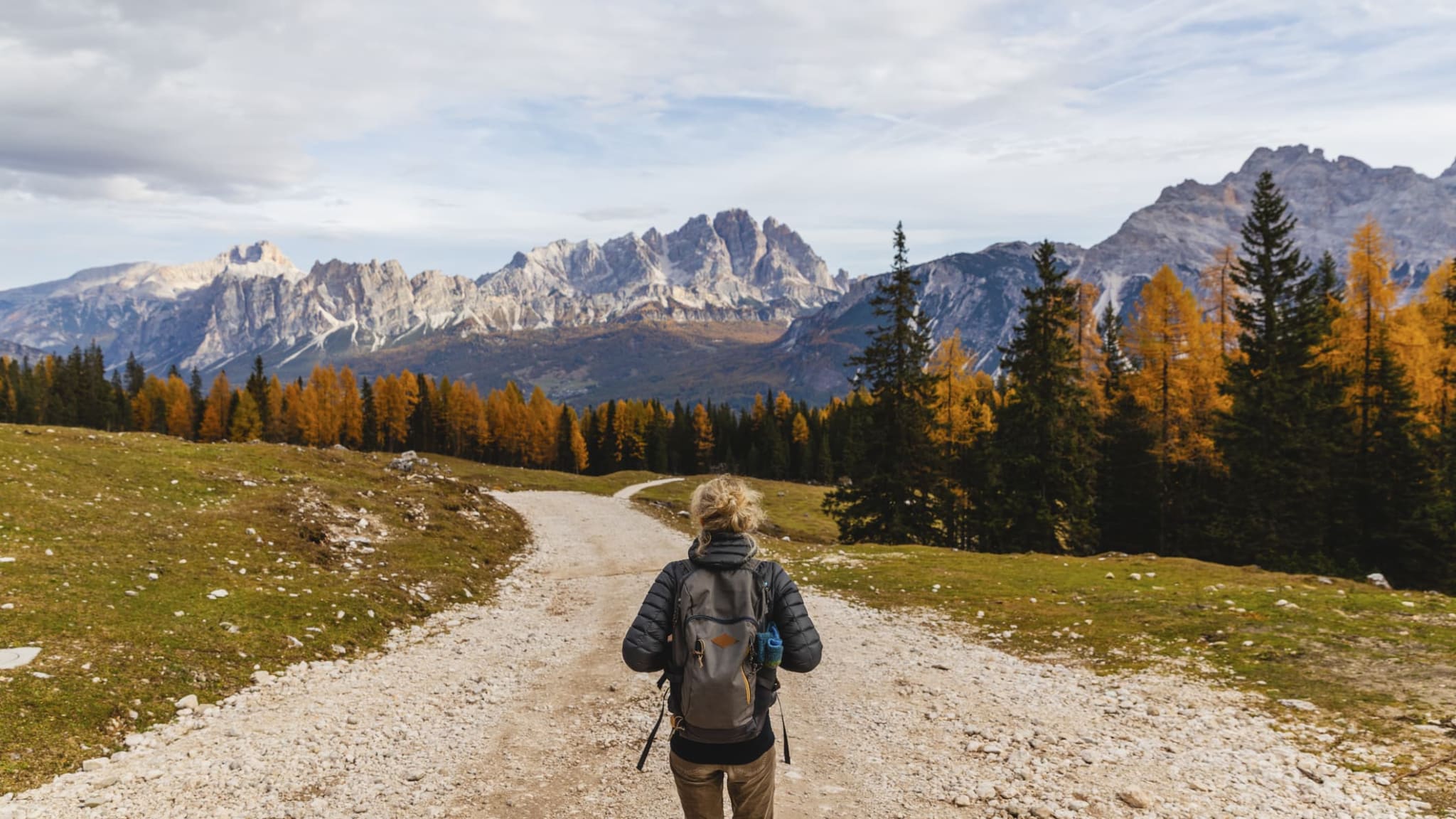 Eine junge Frau wandert auf einem Weg vor den Dolomiten in Italien.