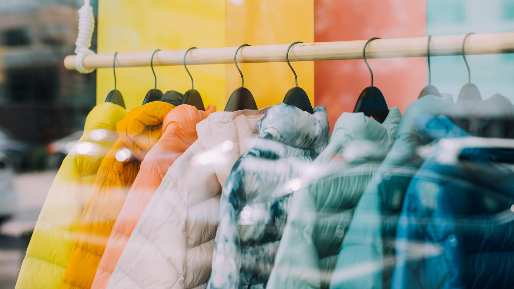 Im Schaufenster eines Kleidungsladens werden bunte Jacken auf einer Stange präsentiert