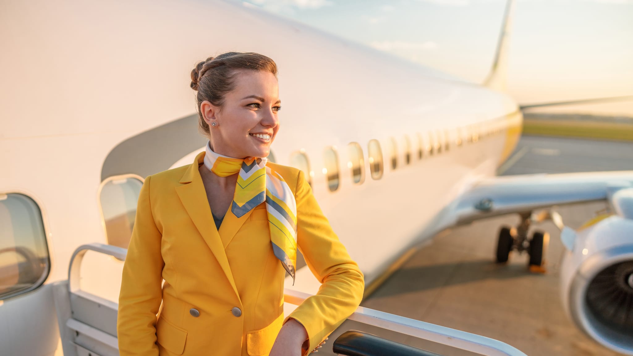 Eine FlugbegleiterIn in gelber Uniform mit Halstuch vor einem Flugzeug
