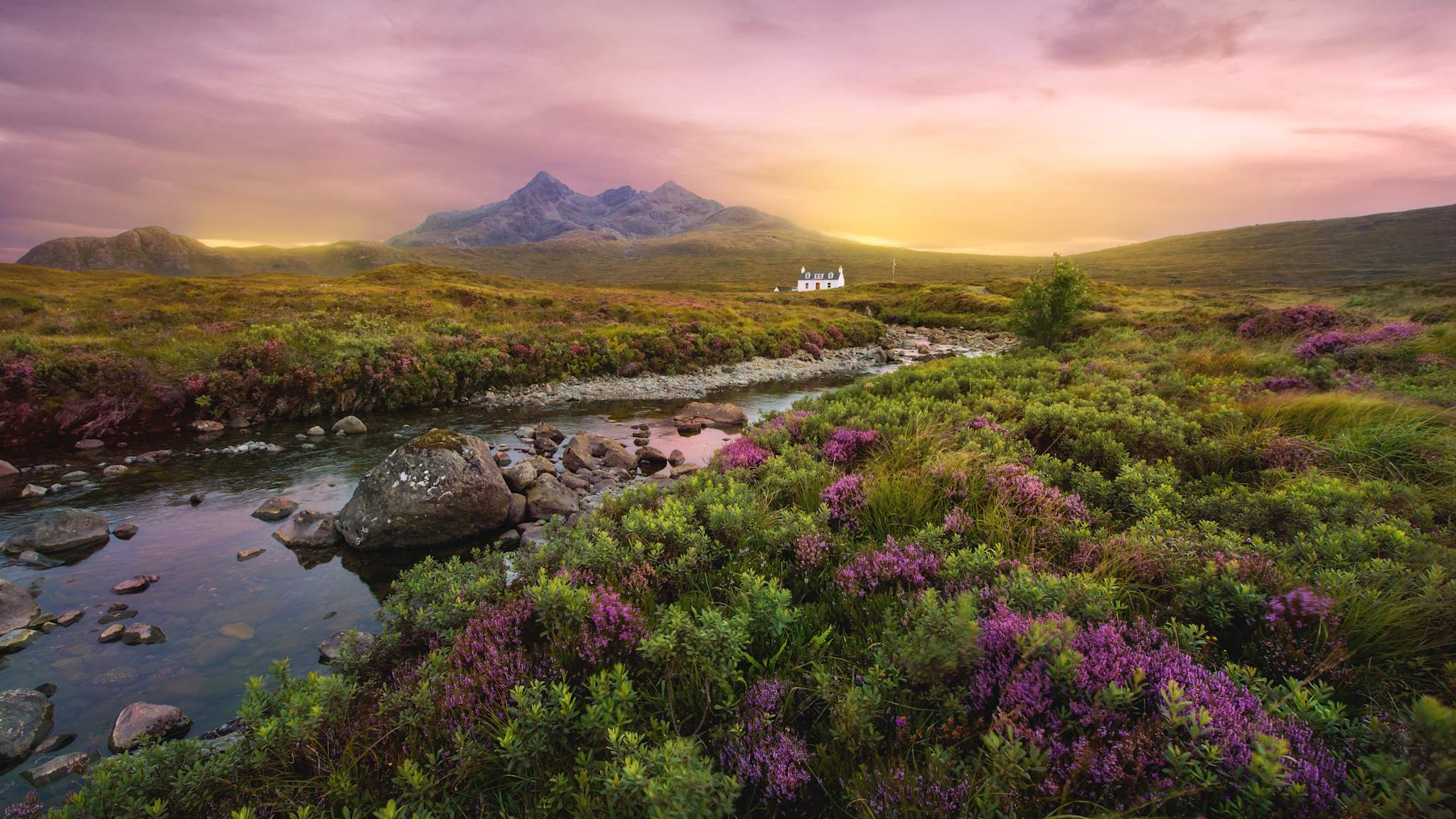 Ein Fluss fließt durch die Landschaft der schottischen Highlands. In der Ferne steht ein weißes Haus.
