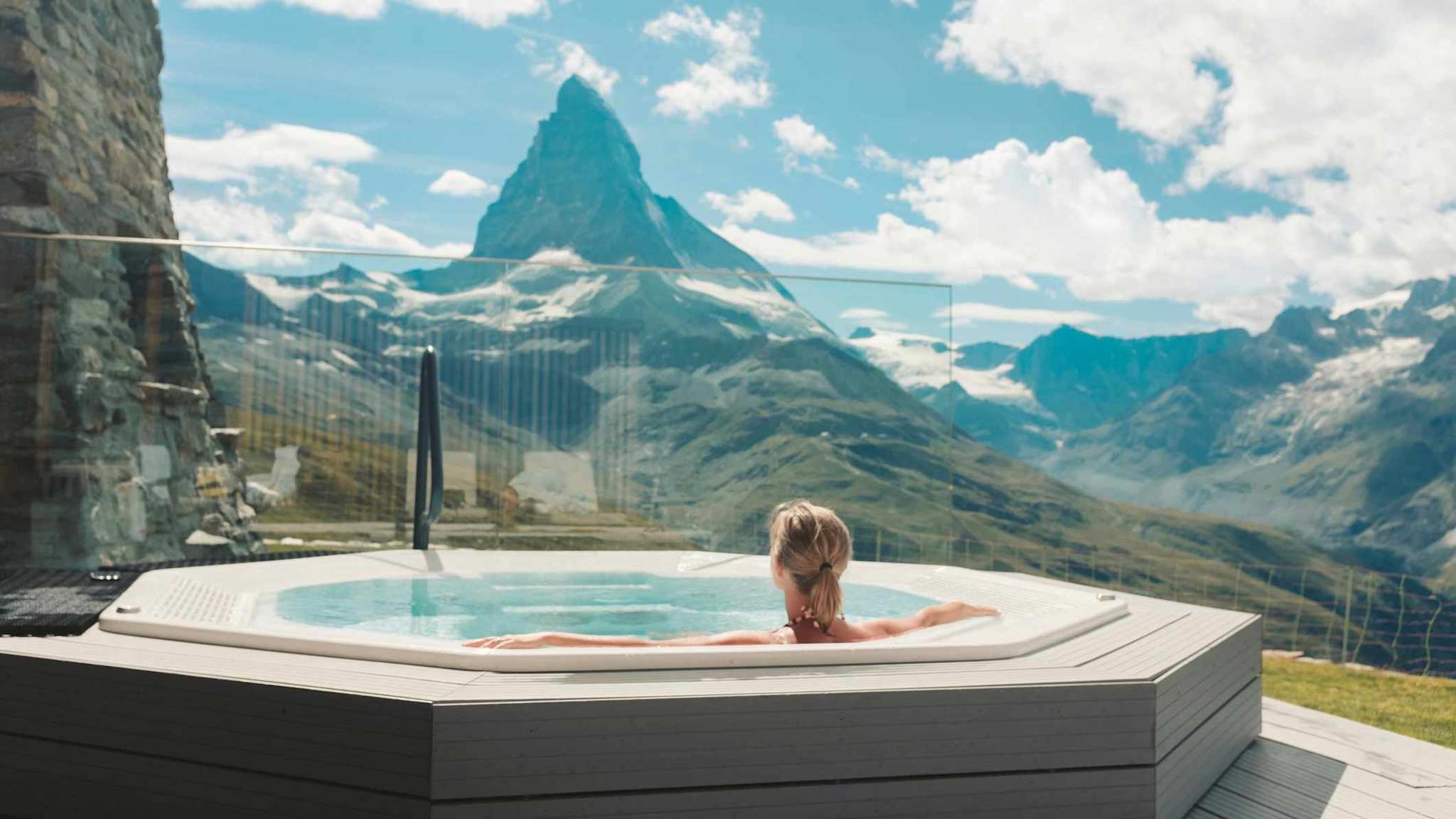 Eine Frau entspannt in einem Whirlpool mit Blick auf die umliegende Berglandschaft.