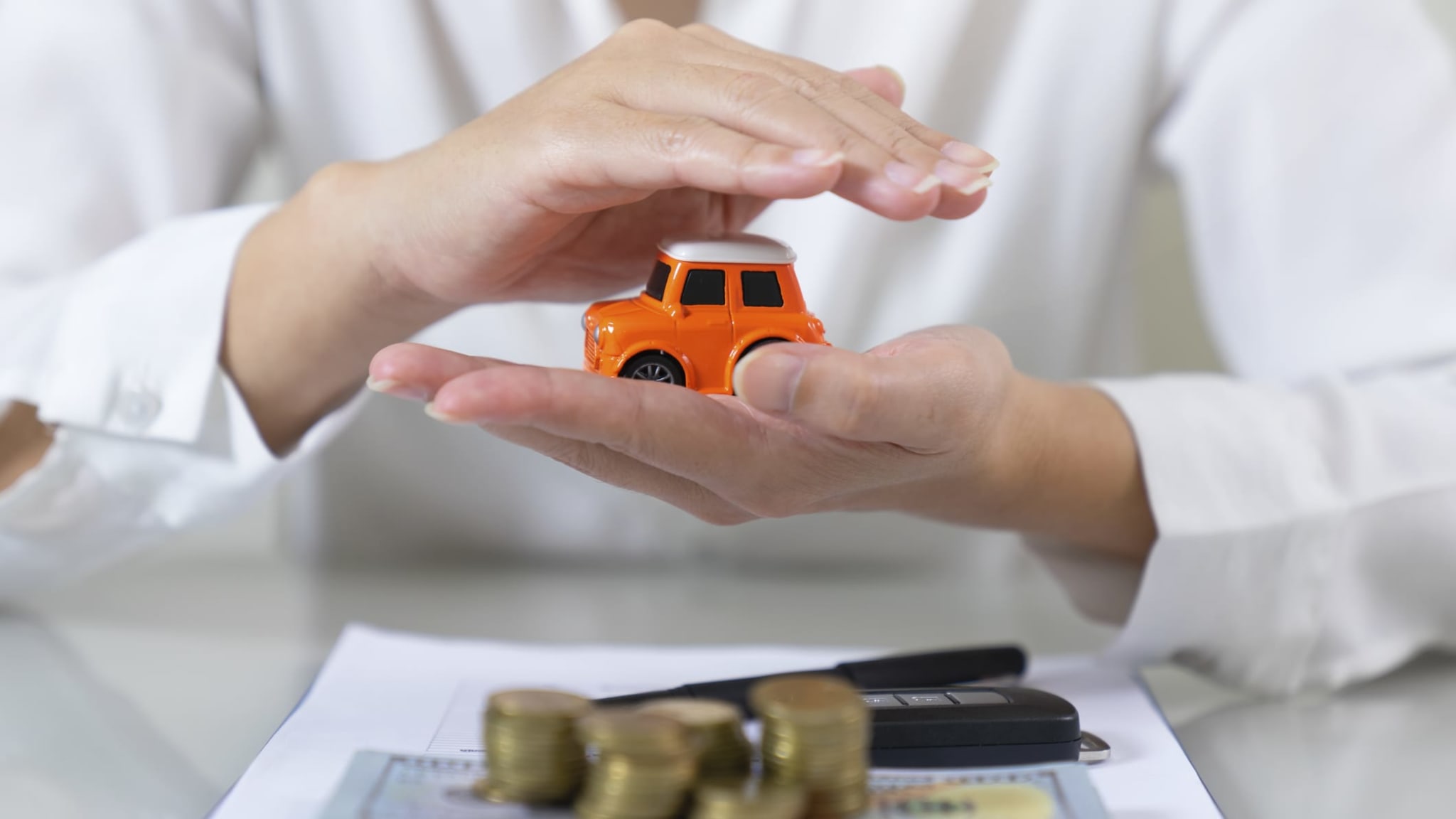 Eine Frau hält ein Spielzeugauto in den Händen, im Vordergrund liegt Geld.