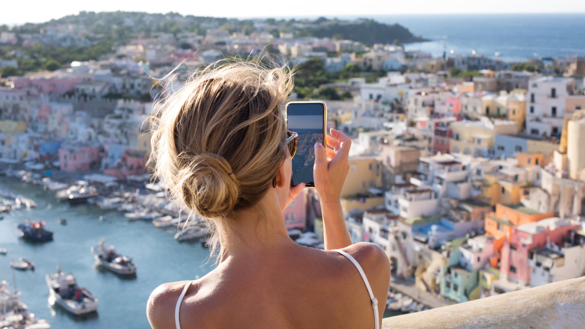 Eine Frau macht Fotos vom Hafen von Corricella in Italien.