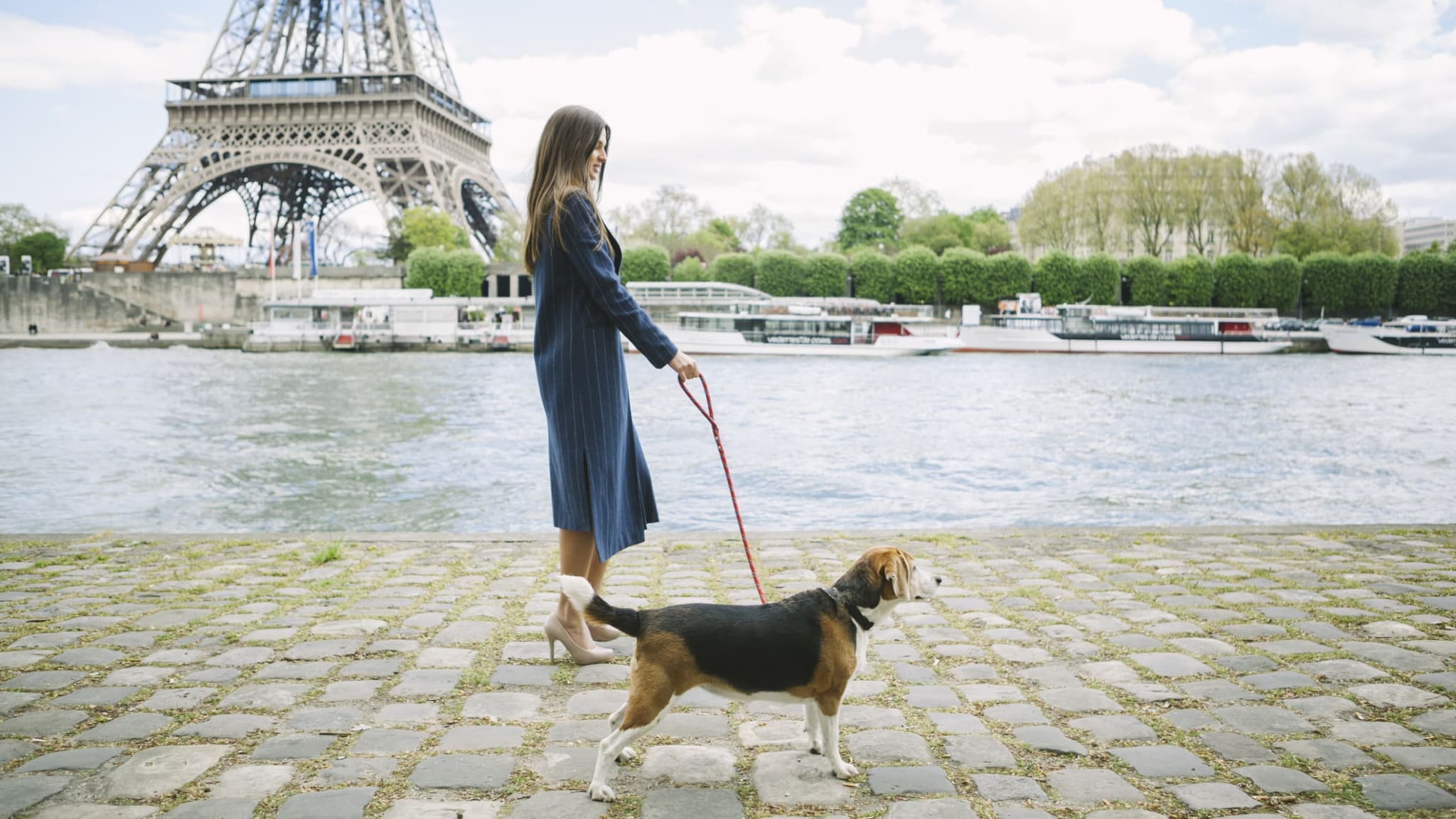 Eine Frau spaziert mit ihrem Hund am Eifelturm in Paris vorbei.