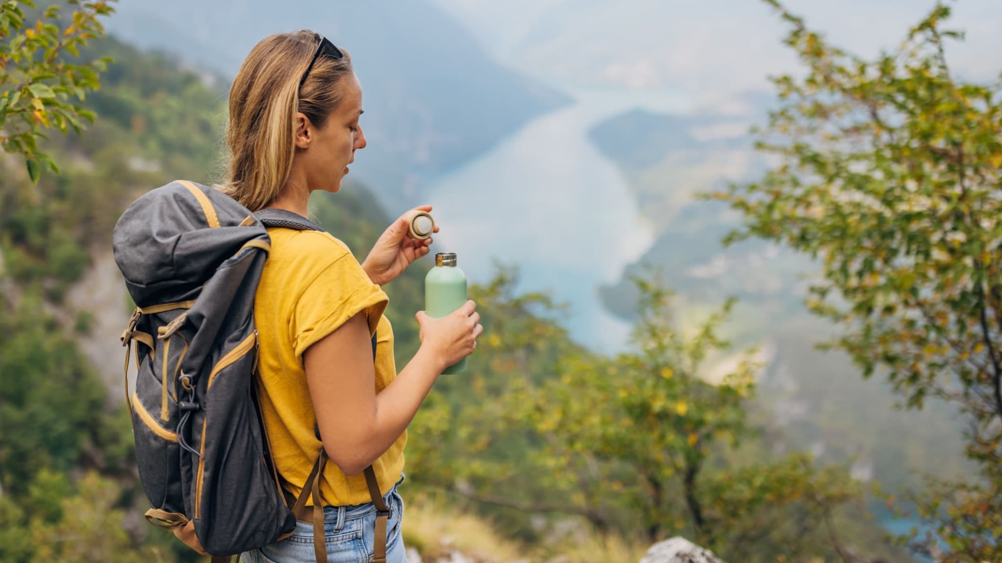 Eine Frau schließt ihre Wasserflasche aus Stahl und genießt den Ausblick von einem Gipfel.