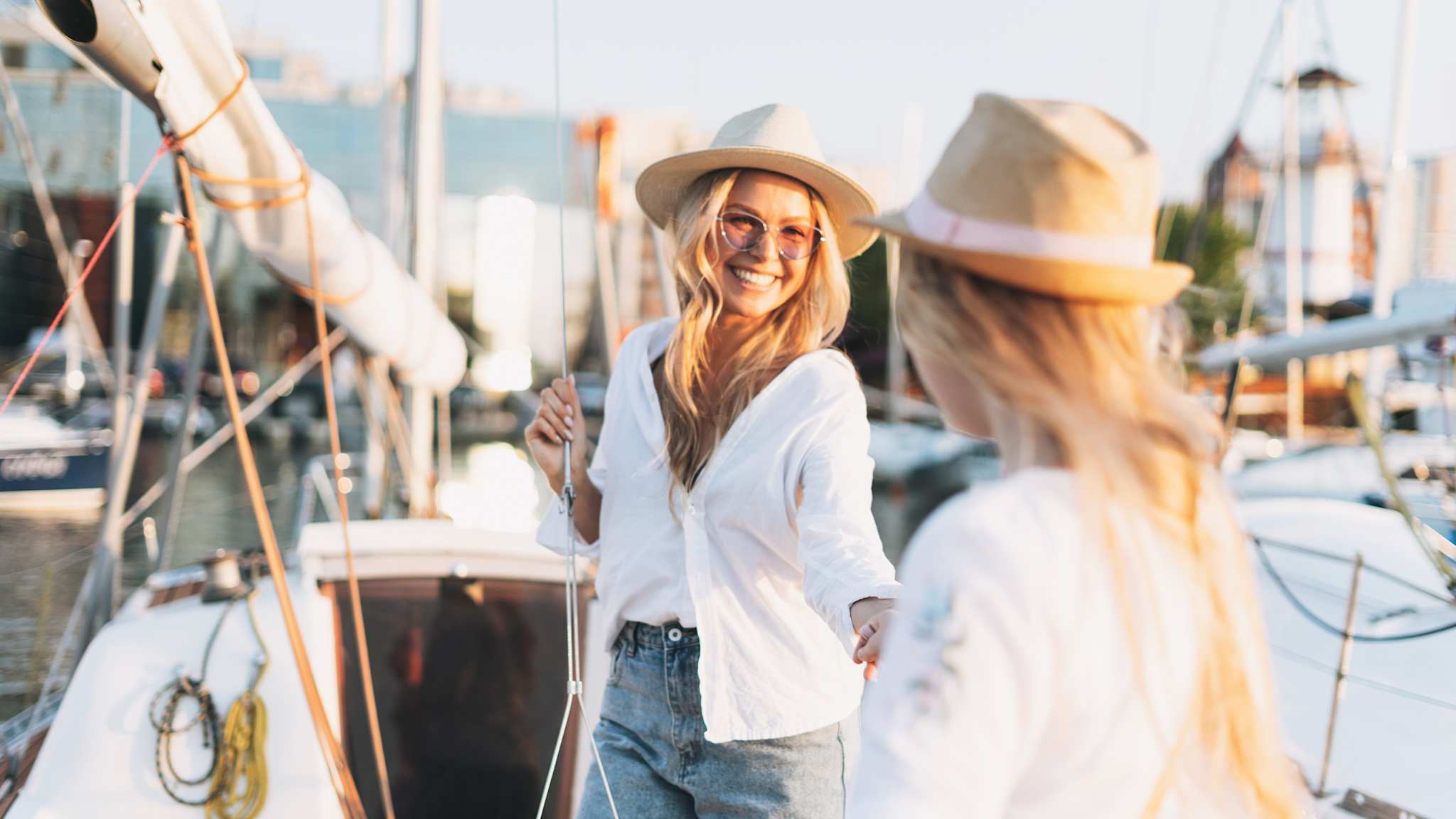 Zwei Frauen mit Hüten halten Hände vor einer Reihe aus Booten
