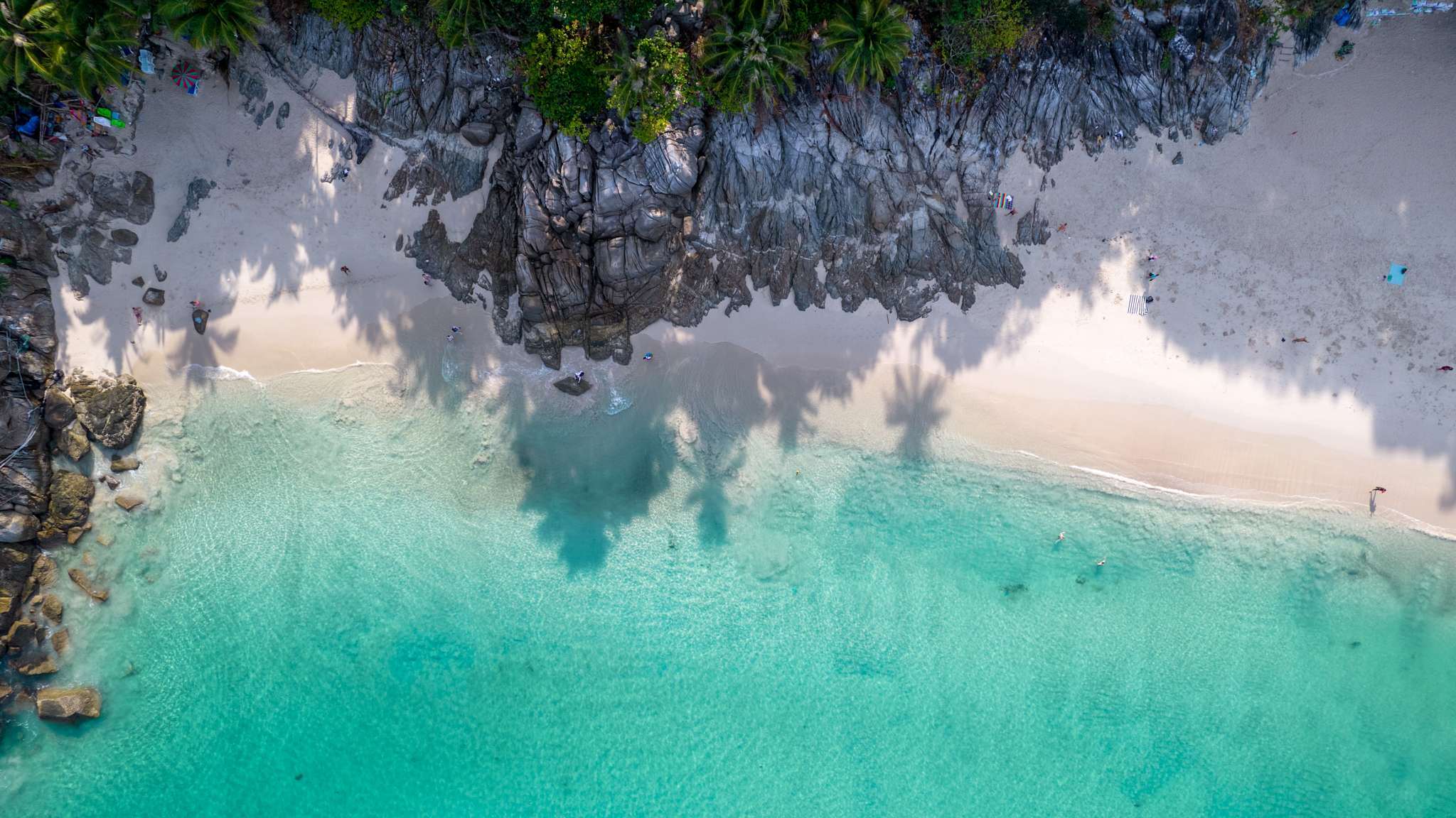 Luftaufnahme eines weißen Sandstandes, der an Meer und Felsen grenzt