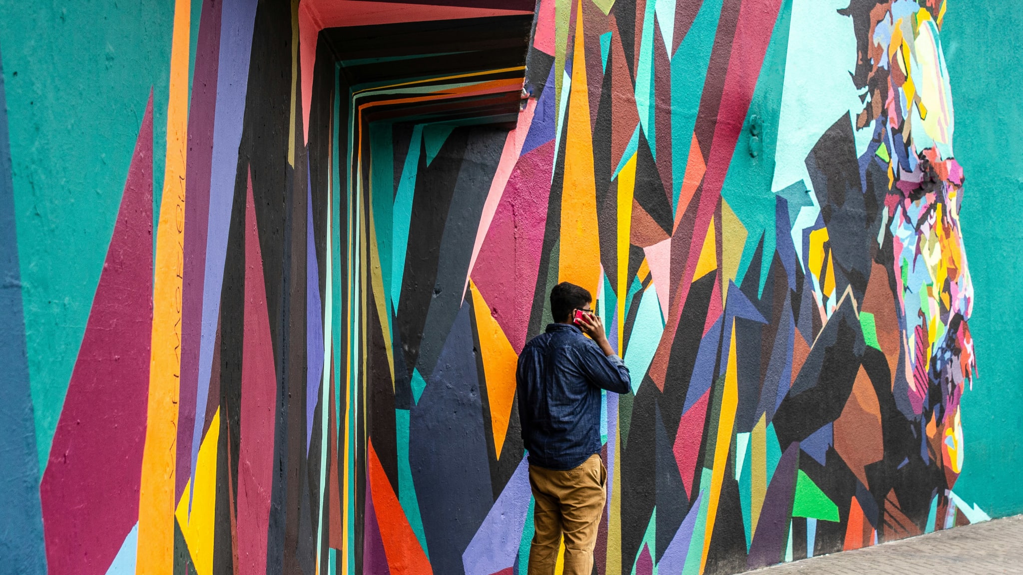 Mann in blauem Hemd und braunen Jeans steht neben Graffiti-Wandkunst