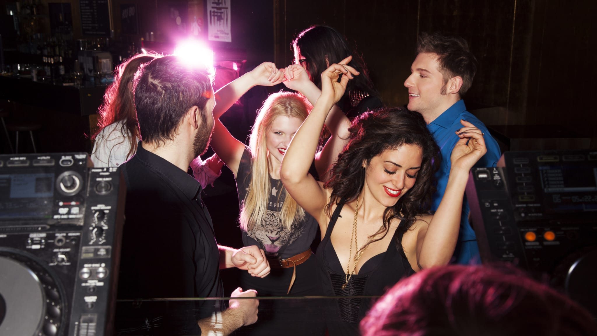 Gruppe von Freunden tanzt vor dem DJ-Pult in Nachtclub. © Manuela/Image Source via Getty Images
