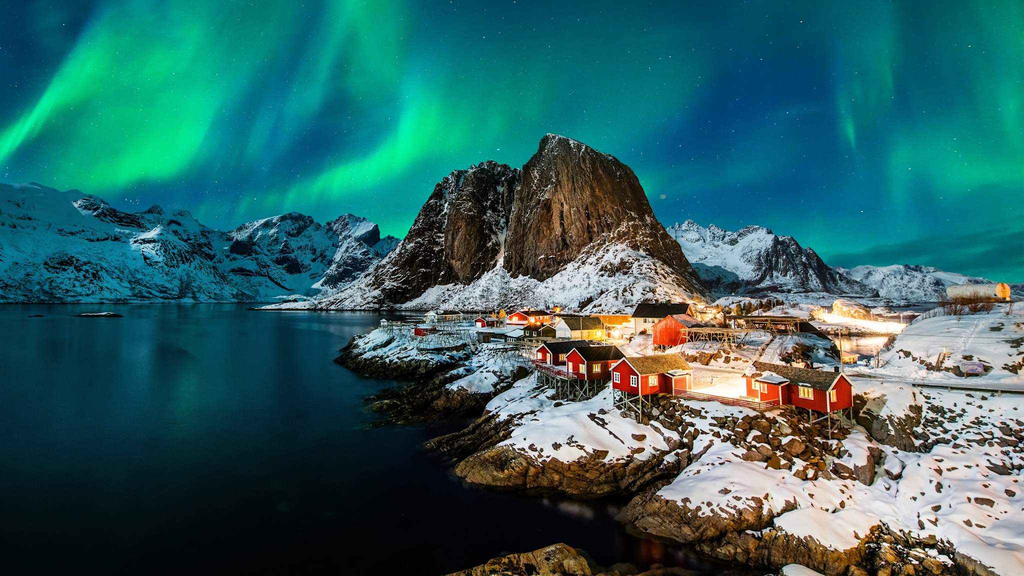 Nordlichter über einer schneebedeckten Felslandschaft mit kleinen roten Häusern.