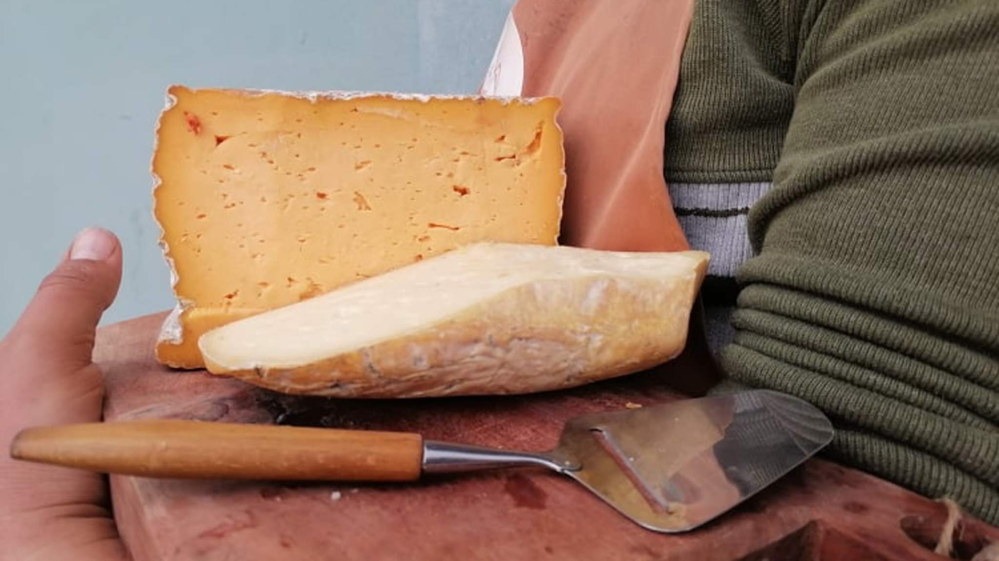 Ein Arm hält ein Brett mit Käse.