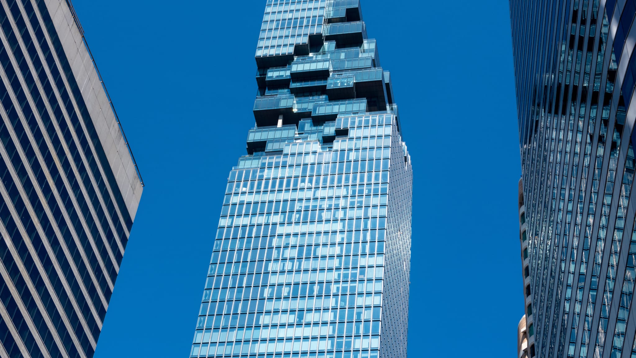 Man sieht einen Wolkenkratzer mit Glasfassade und einer Aussichtsplattform auf dem Dach.