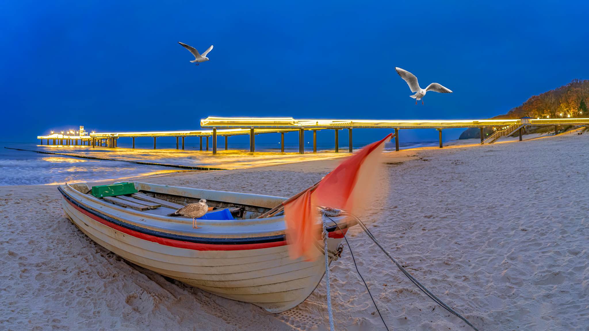 Ein Boot liegt am Strand vor einer beleuchteten Seebrücke.