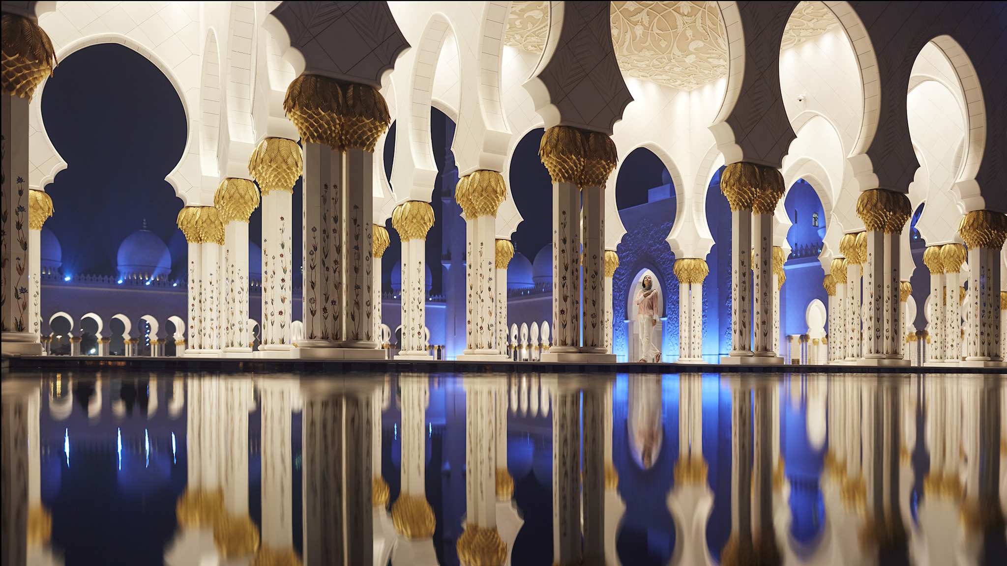 Die Säulen einer Moschee bei Nacht, welche sich im Wasser auf dem Boden spiegeln