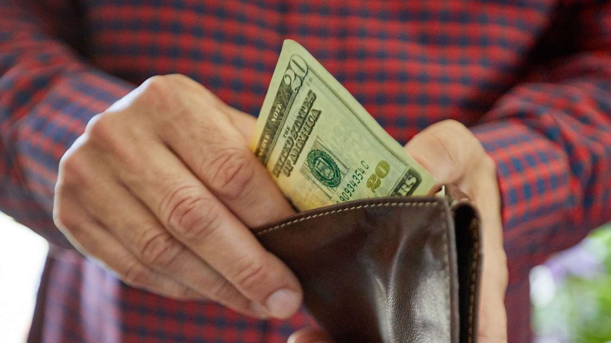 Eine Männerhand packt Dollarscheine in ein Portemonaie.