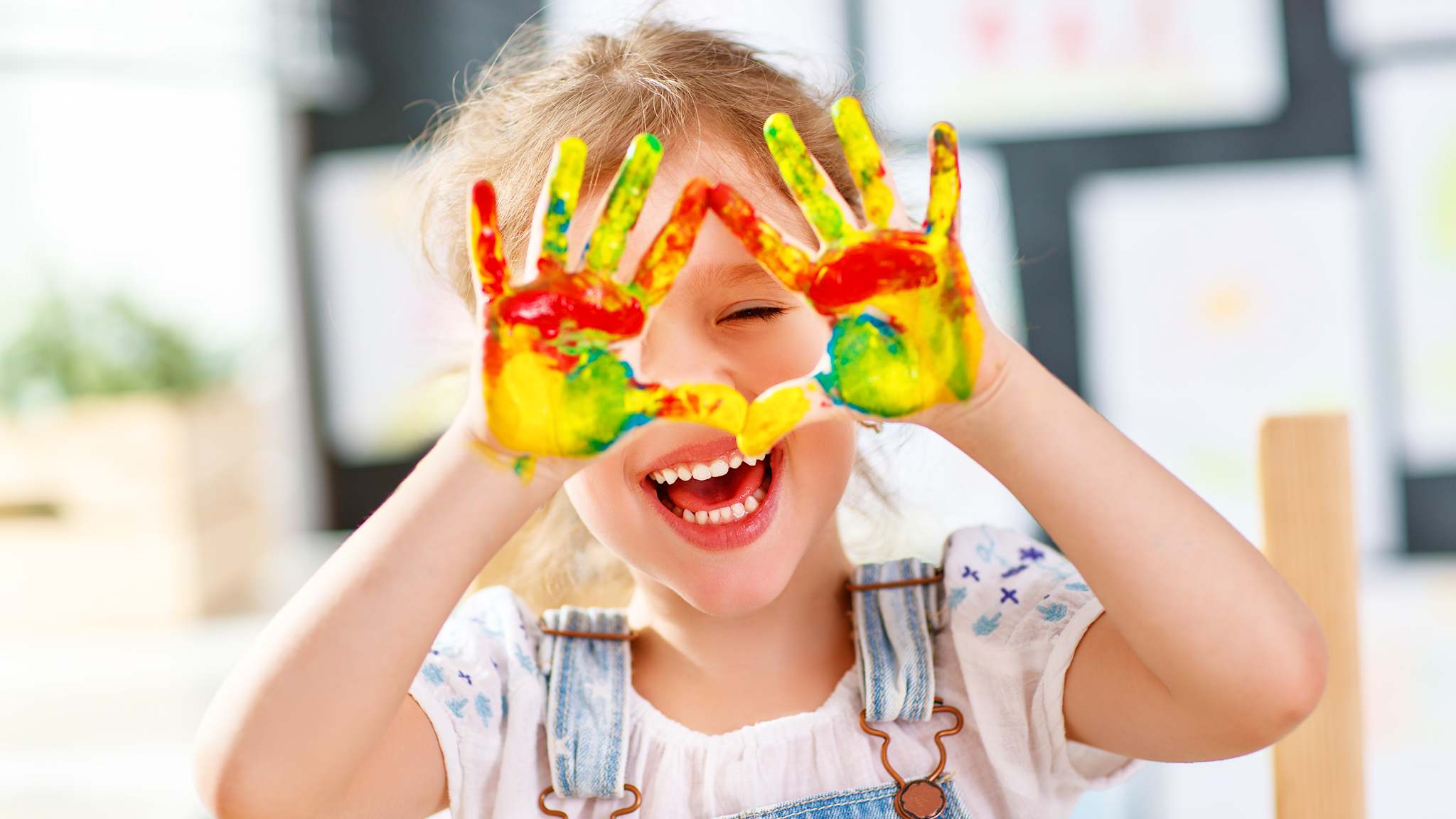 Ein Kind hält lachend bunte Hände voller Farbe in die Kamera