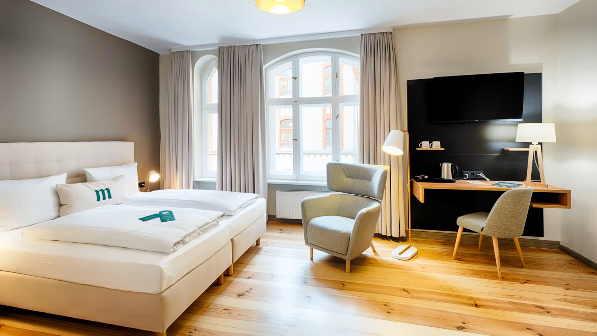 Doppelzimmer mit Sessel, Fernseher und Arbeitsecke.