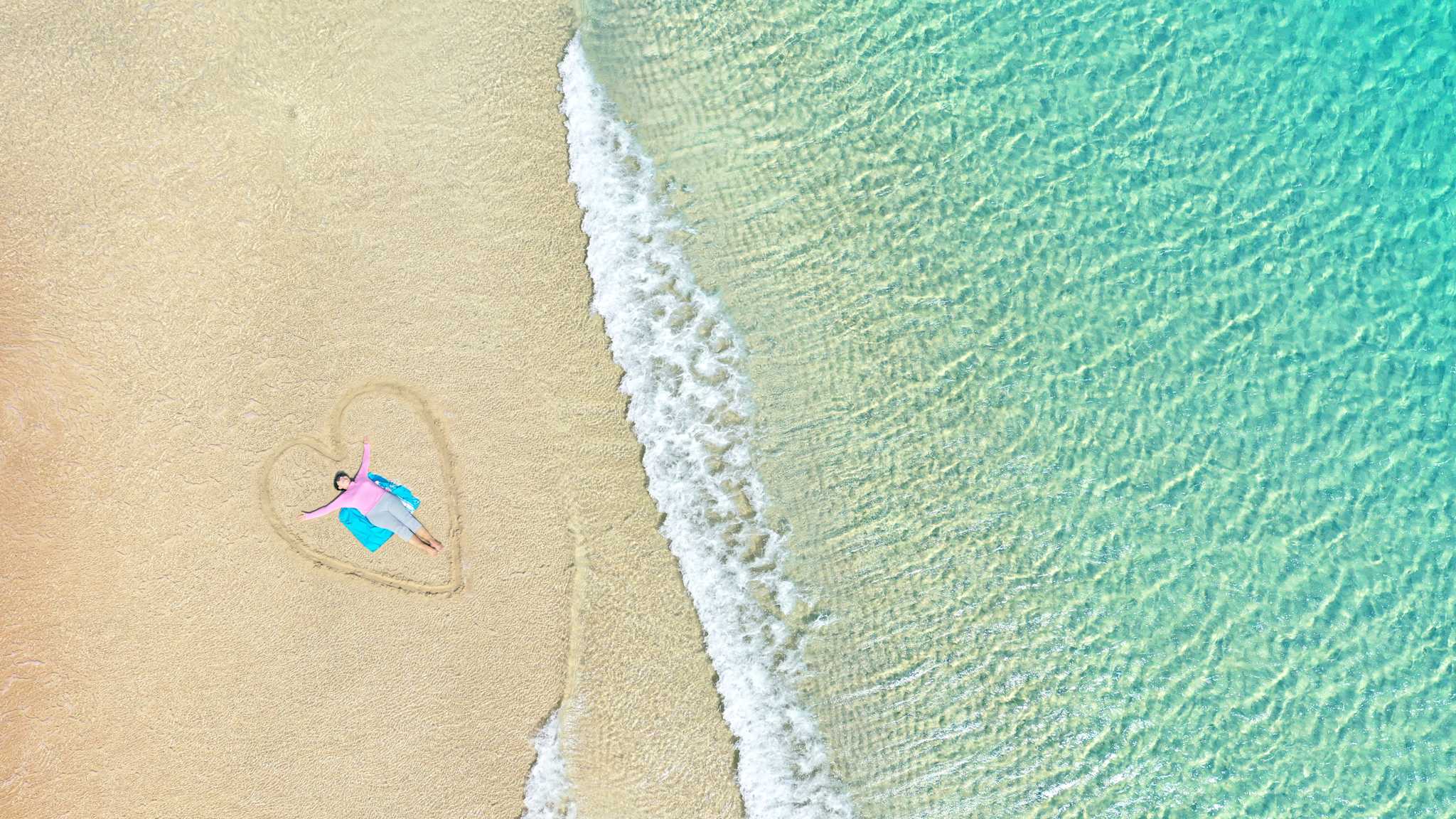 Eine Frau liegt am Strand in einem in den Sand gezeichneten Herz