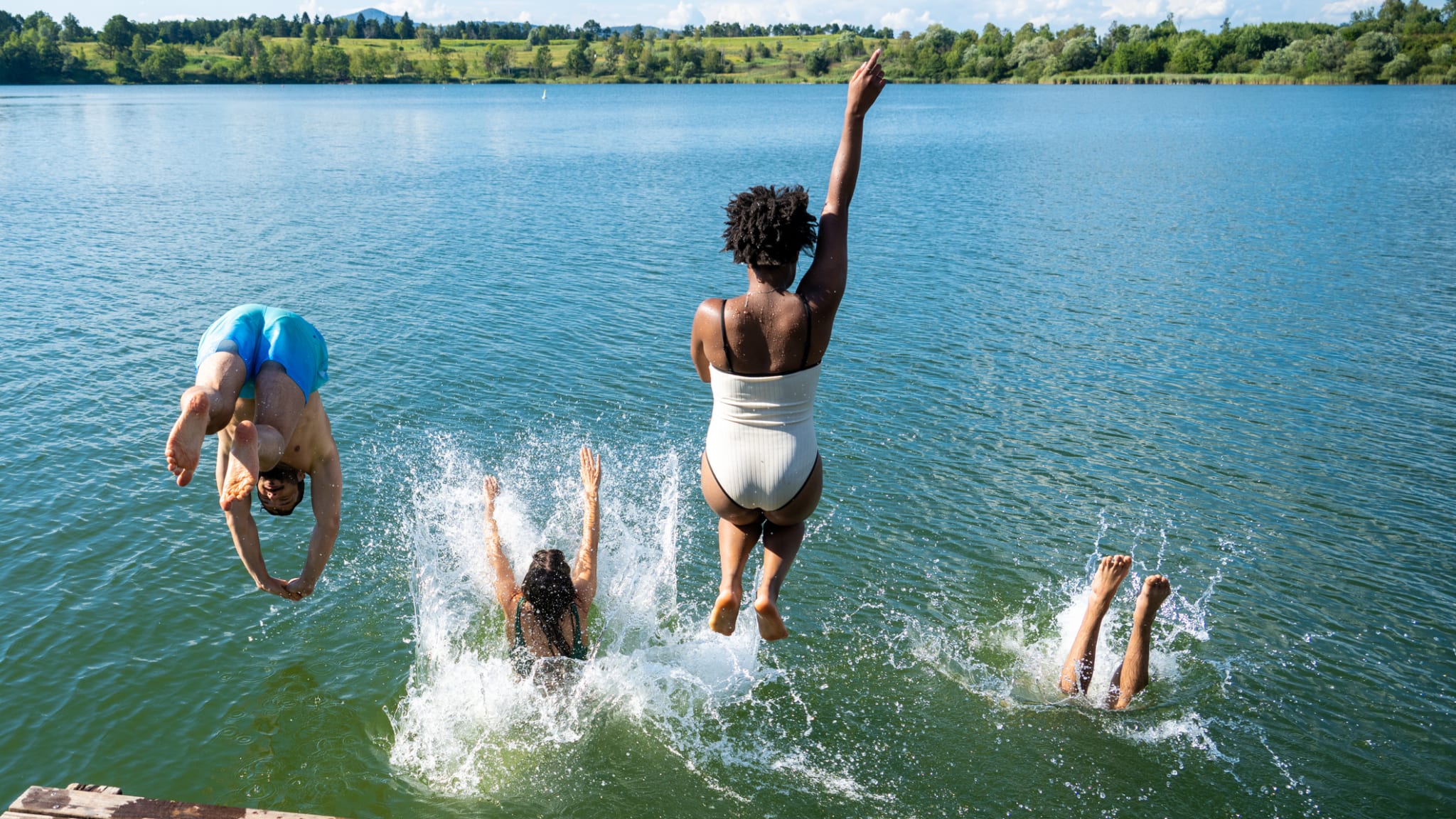 Mehrere Personen springen in das Wasser eines Sees