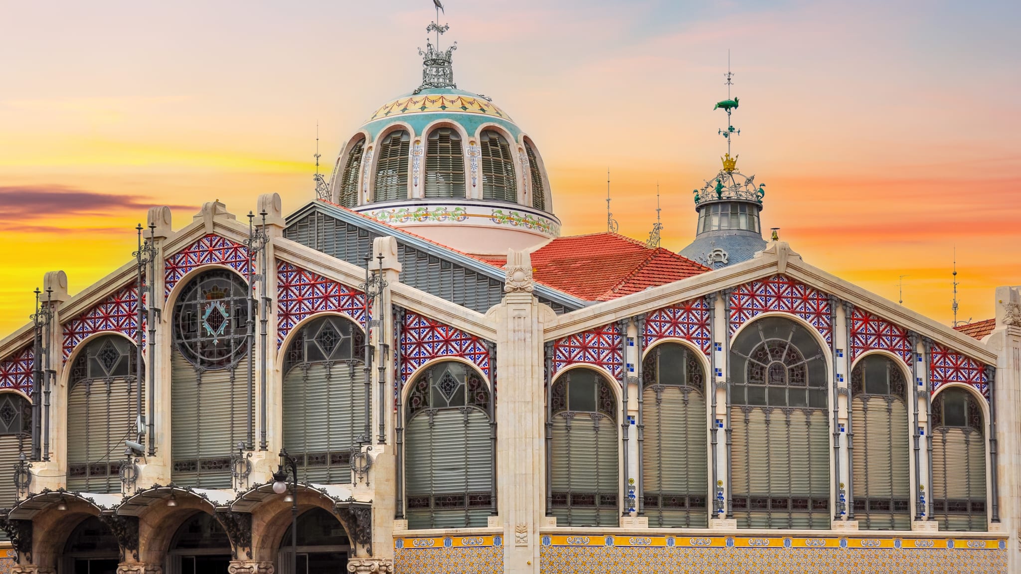 Blick auf das architektonisch spannende Marktgebäude in Valencia. Der Markt hat zwei runde Kuppeln, und große Fenster mit Rundbögen und ist reich mit Mosaik verziert.