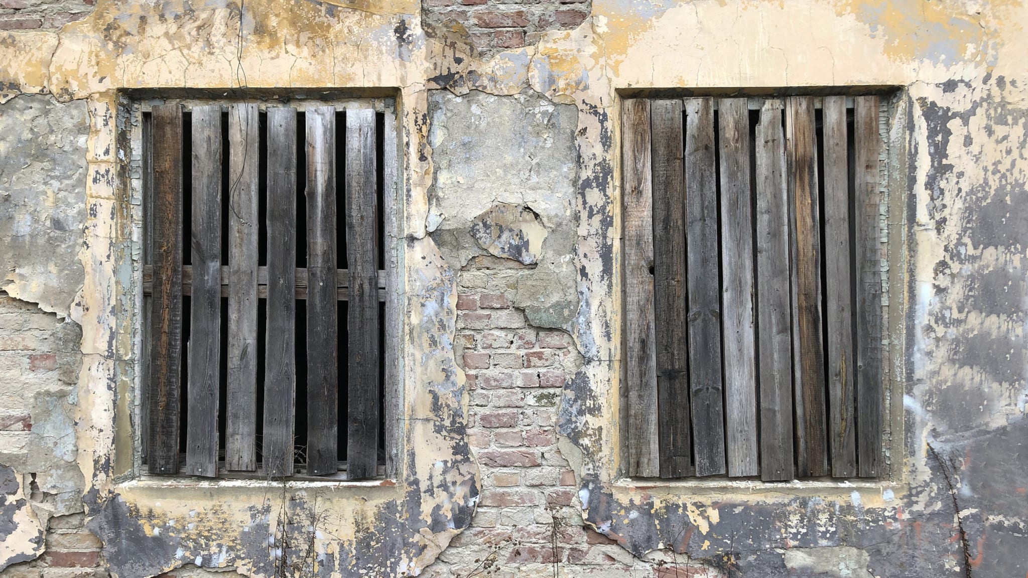 Mit Holzbrettern verschlossene Fenster eines alten Steinhauses.