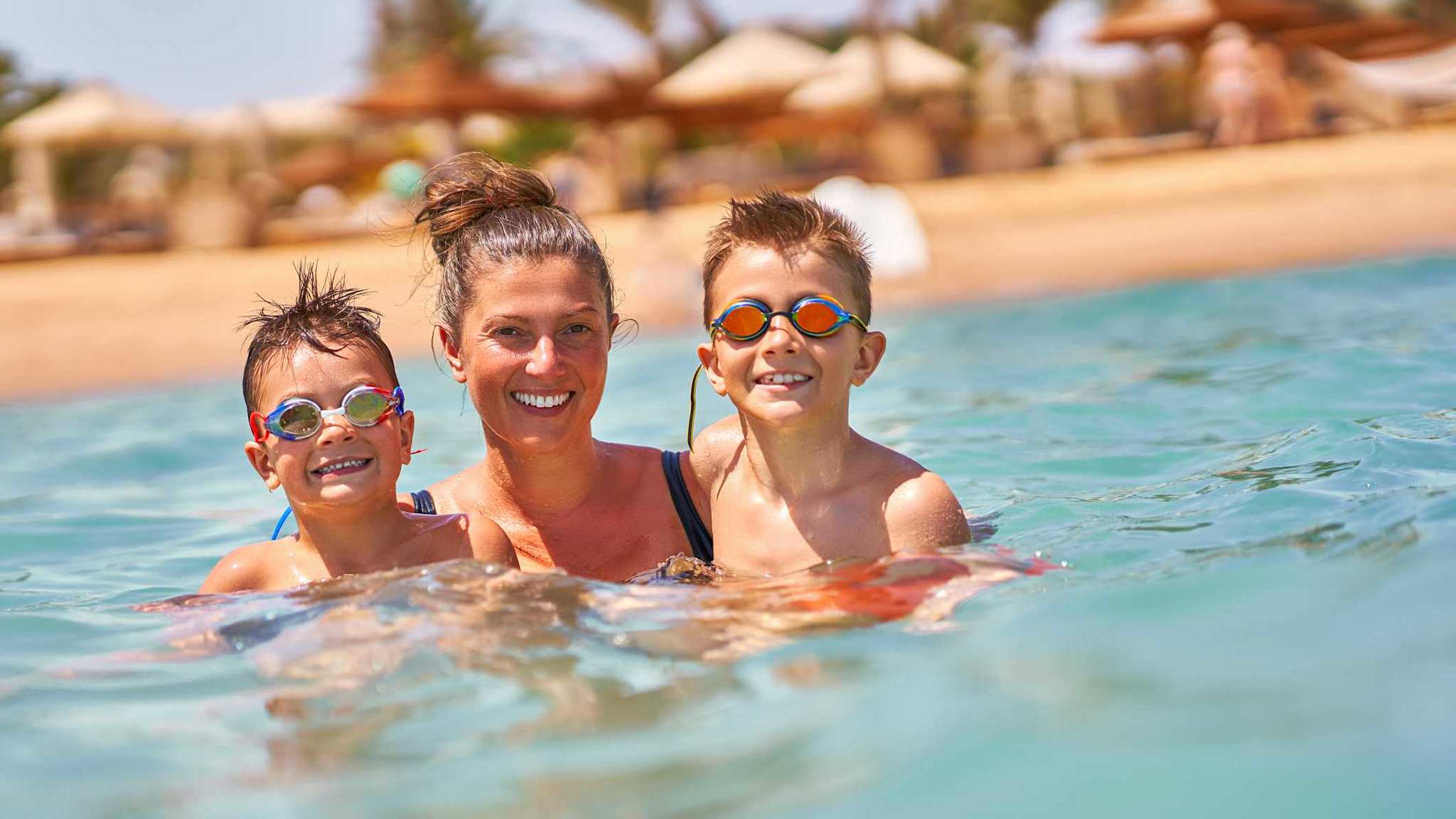 Eine Mutter schwimmt mit ihren beiden Söhnen im Meer und haben Spaß.