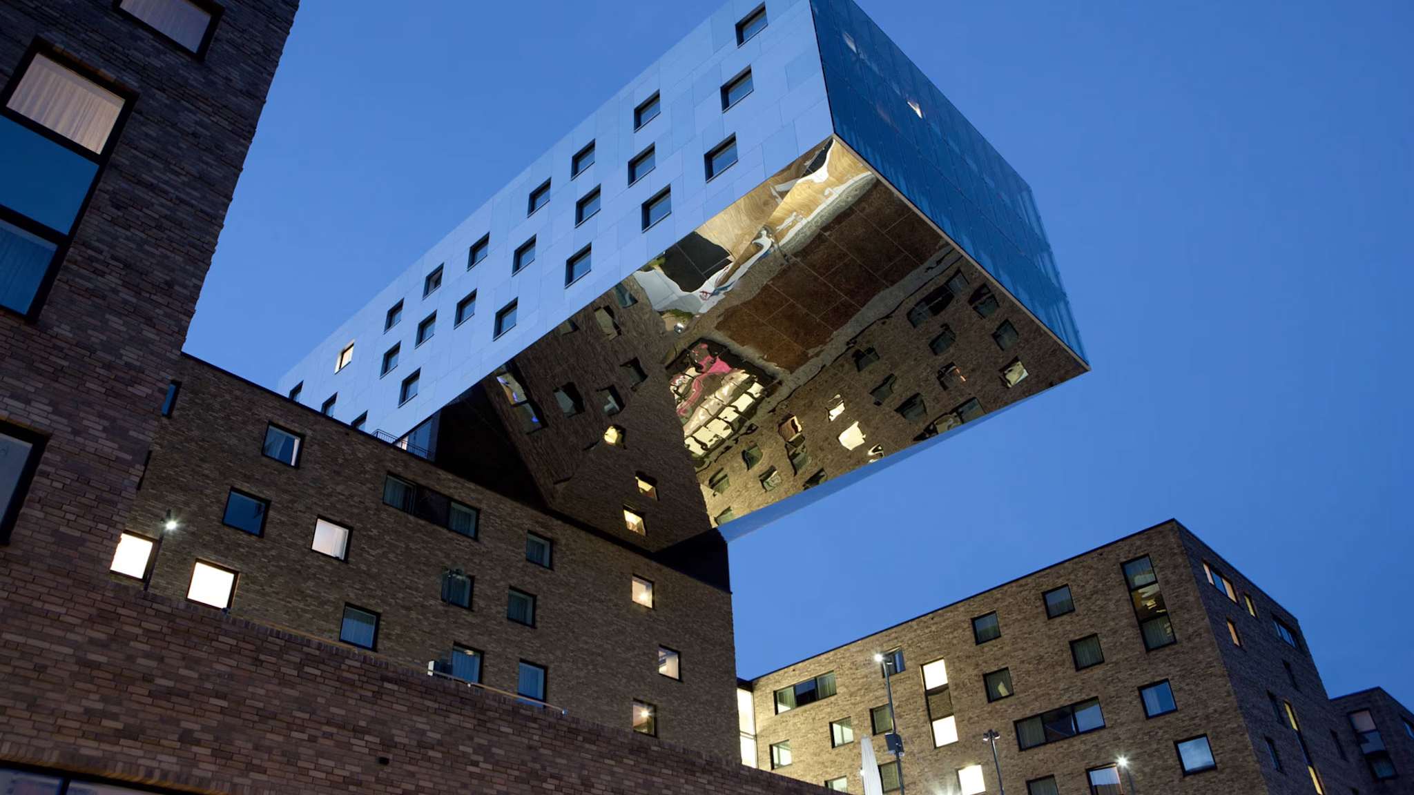 Futuristisches Hotelgebäude nhow Berlin mit verspiegeltem Würfel über Backsteinbauten, abends aufgenommen.