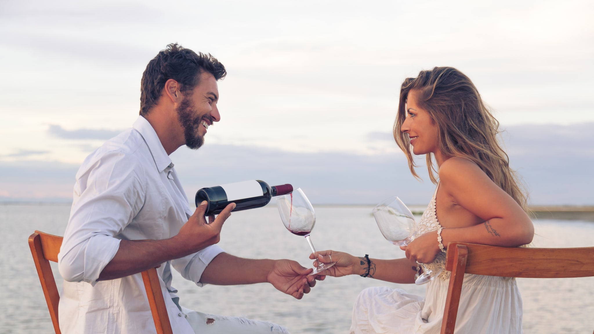 Paar am Strand, Mann gießt Wein in ein Glas ein in Griechenland