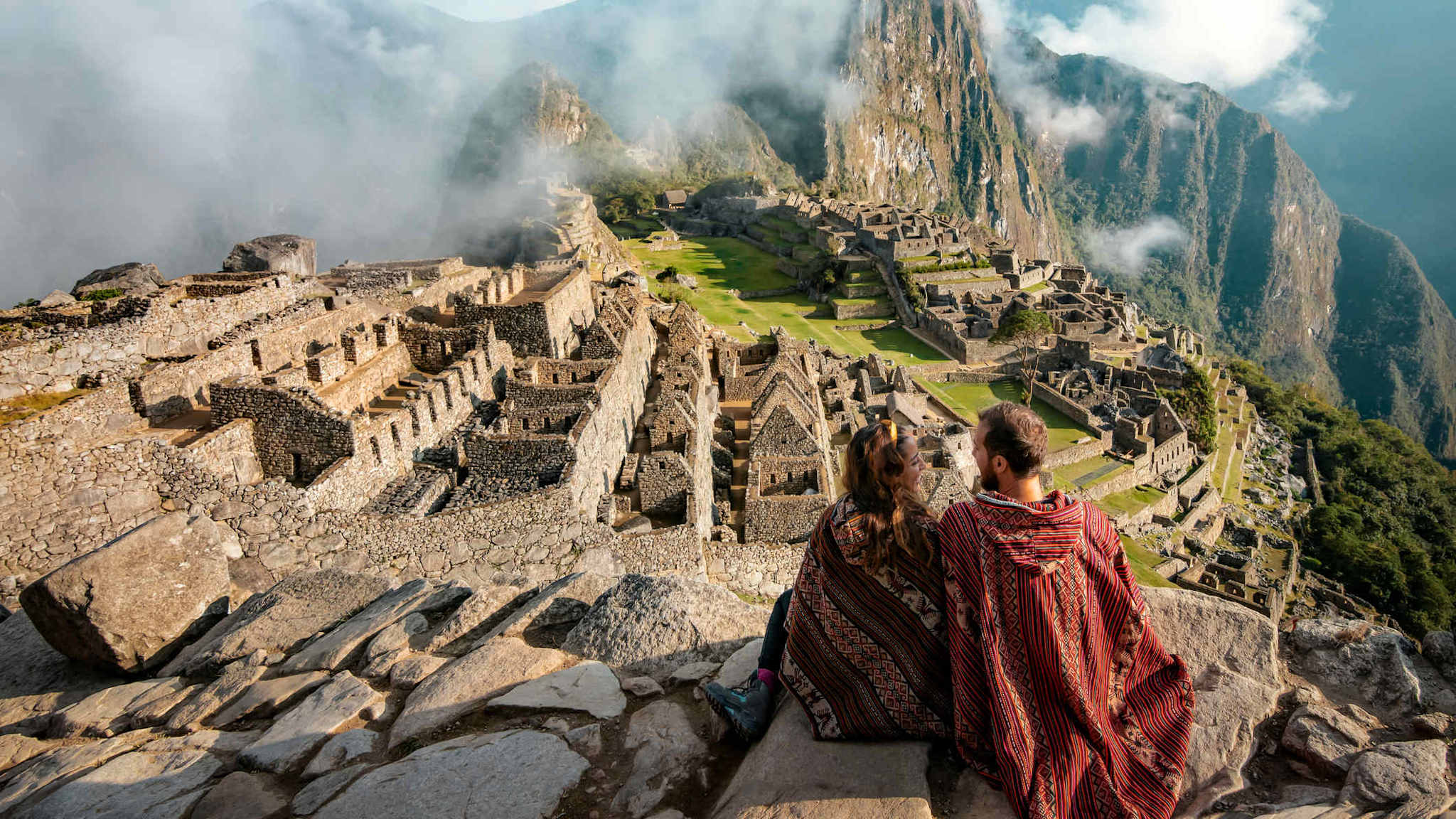 Ein Pärchen in Ponchos gekleidet beobachtet die Ruinen im Machu Picchu, Peru.