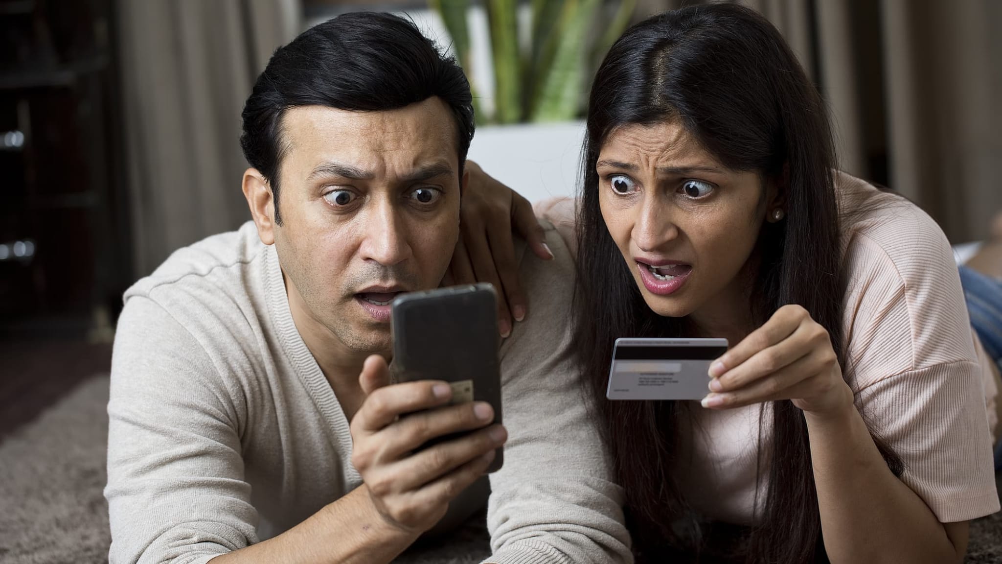 Ein Paar schaut geschockt auf Handy und Kreditkarte.
