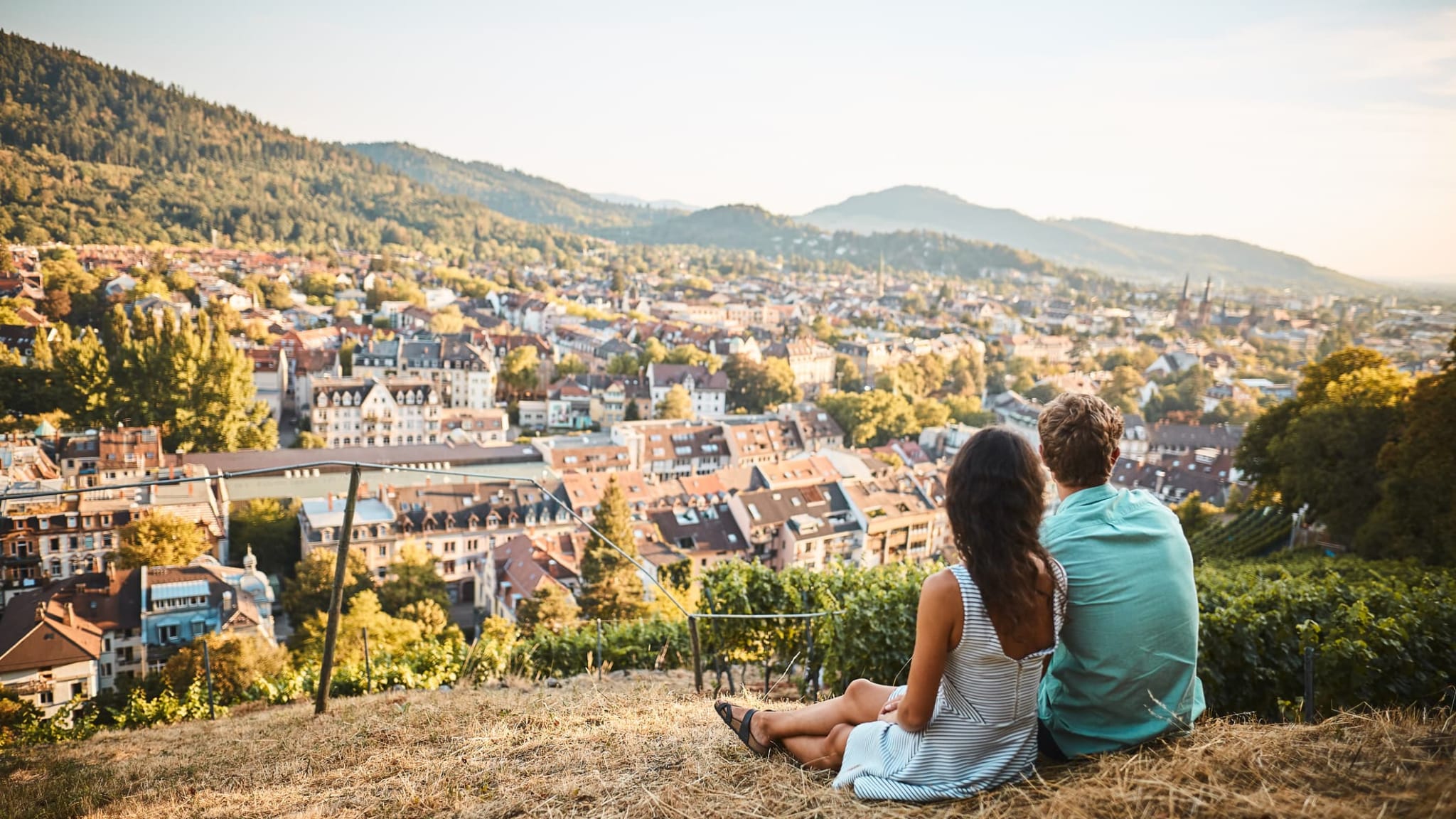 Ein Paar sitzt in den Weinbergen und schaut auf die Stadt.