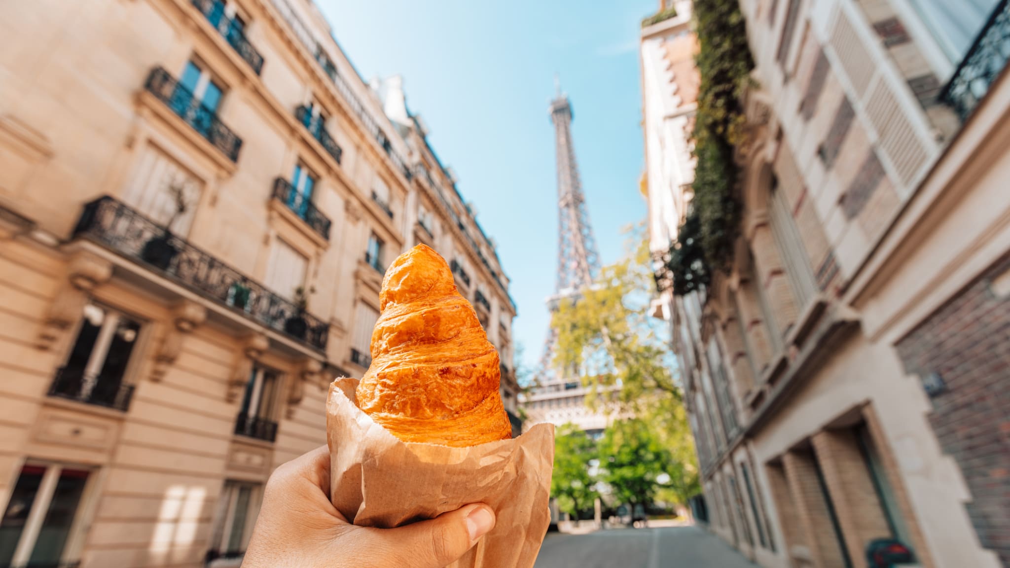 Eine Person mit einem Croissant vor dem Eiffelturm in Paris, Frankreich © Alexander Spatari/Moment via Getty Images