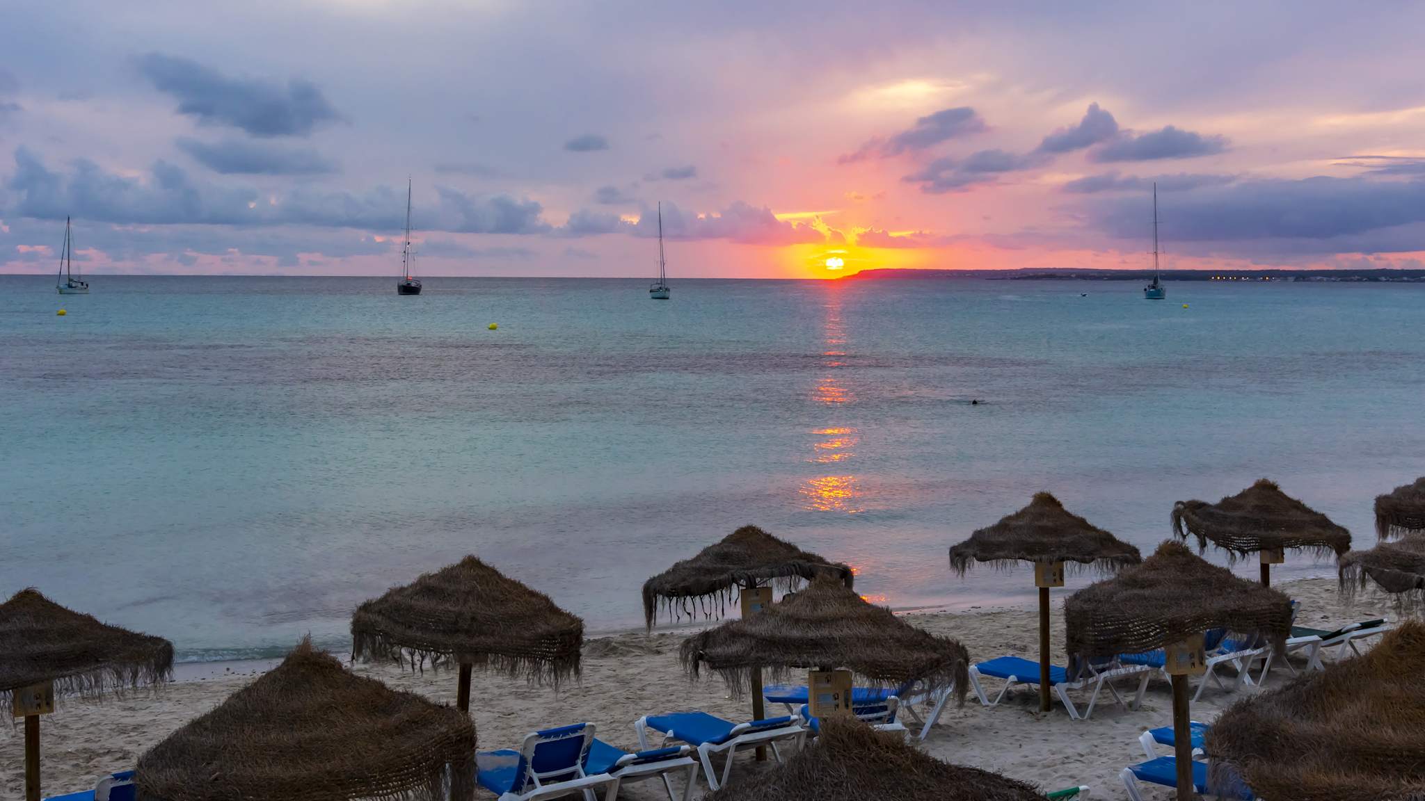 Ein Strand mit Strohsonnenschirmen bei Sonnenuntergang