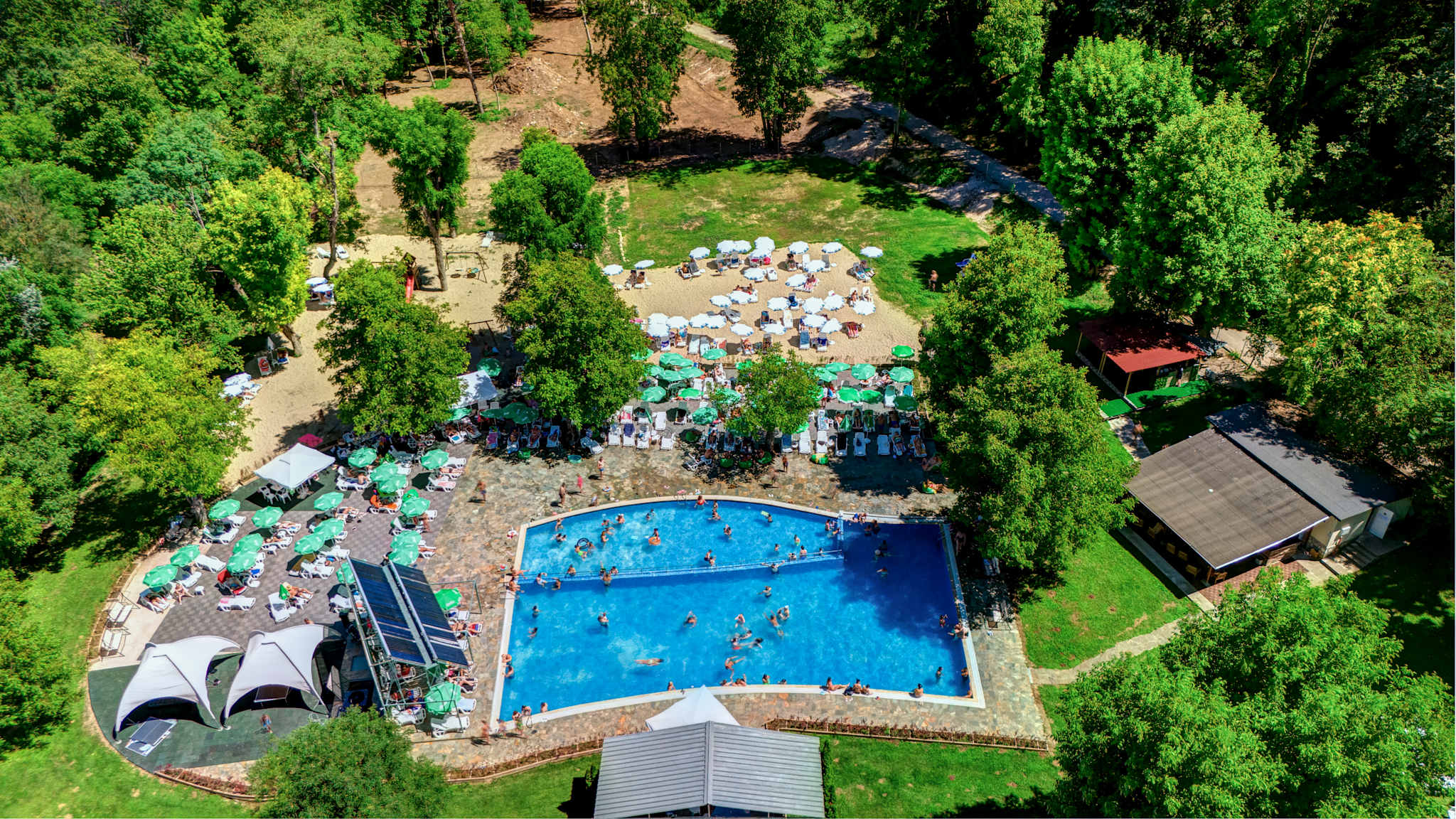 Draufsicht auf einen Pool. Drumherum sind Sonnenschirme und viele Bäume.