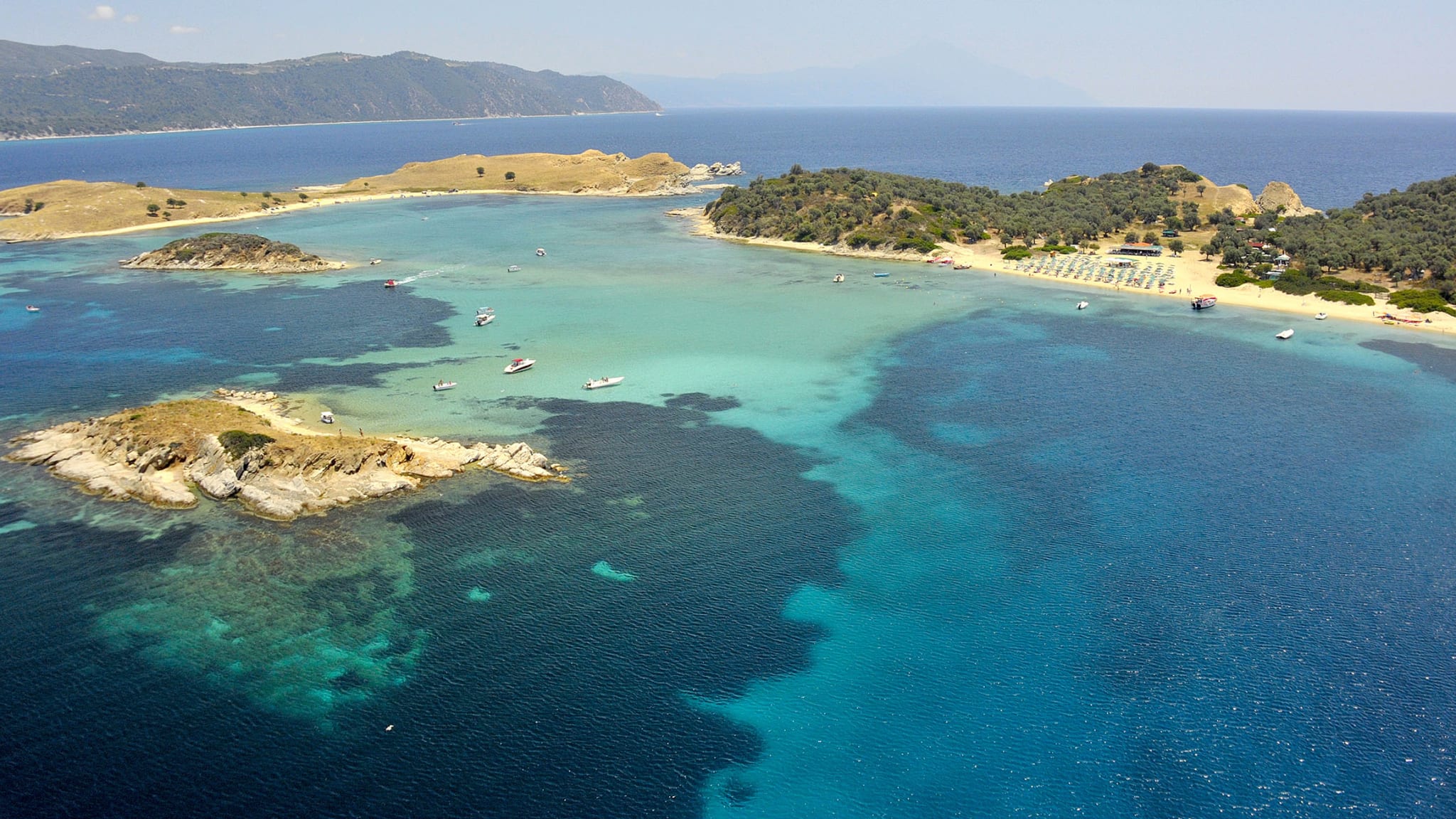 Die Drenia Inseln befinden sich im Meer. Im HIntergrund ist das griechische Festland zu erkennen. Zwischen den kleinen Inseln sind Boote im Wasser.