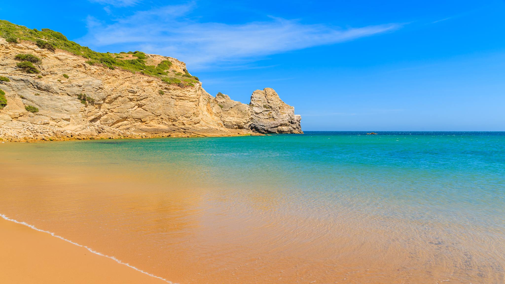 Der Strand von Praia do Barranco hat leuchtend gelben Sand und läuft seicht ins Meer.