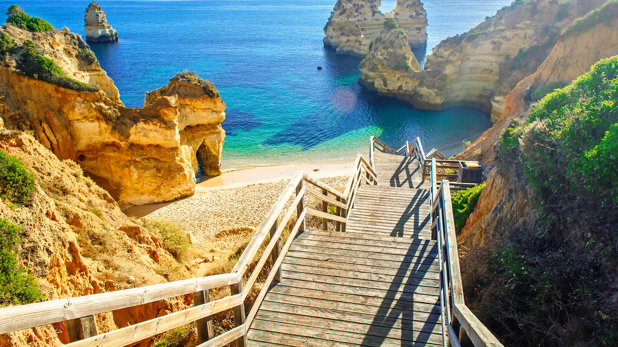 Eine Holzbrücke führt zu einem Strand zwischen Felsen