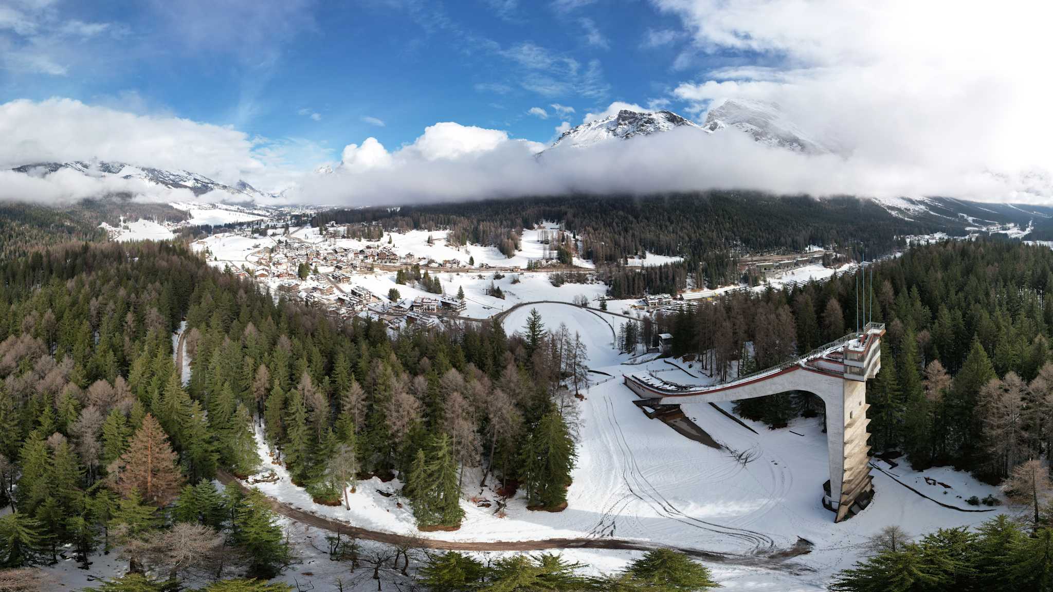 Luftaufnahme mit Blick auf eine alte Sprungschanze in einem bewaldeten Gebiet in den Alpen.