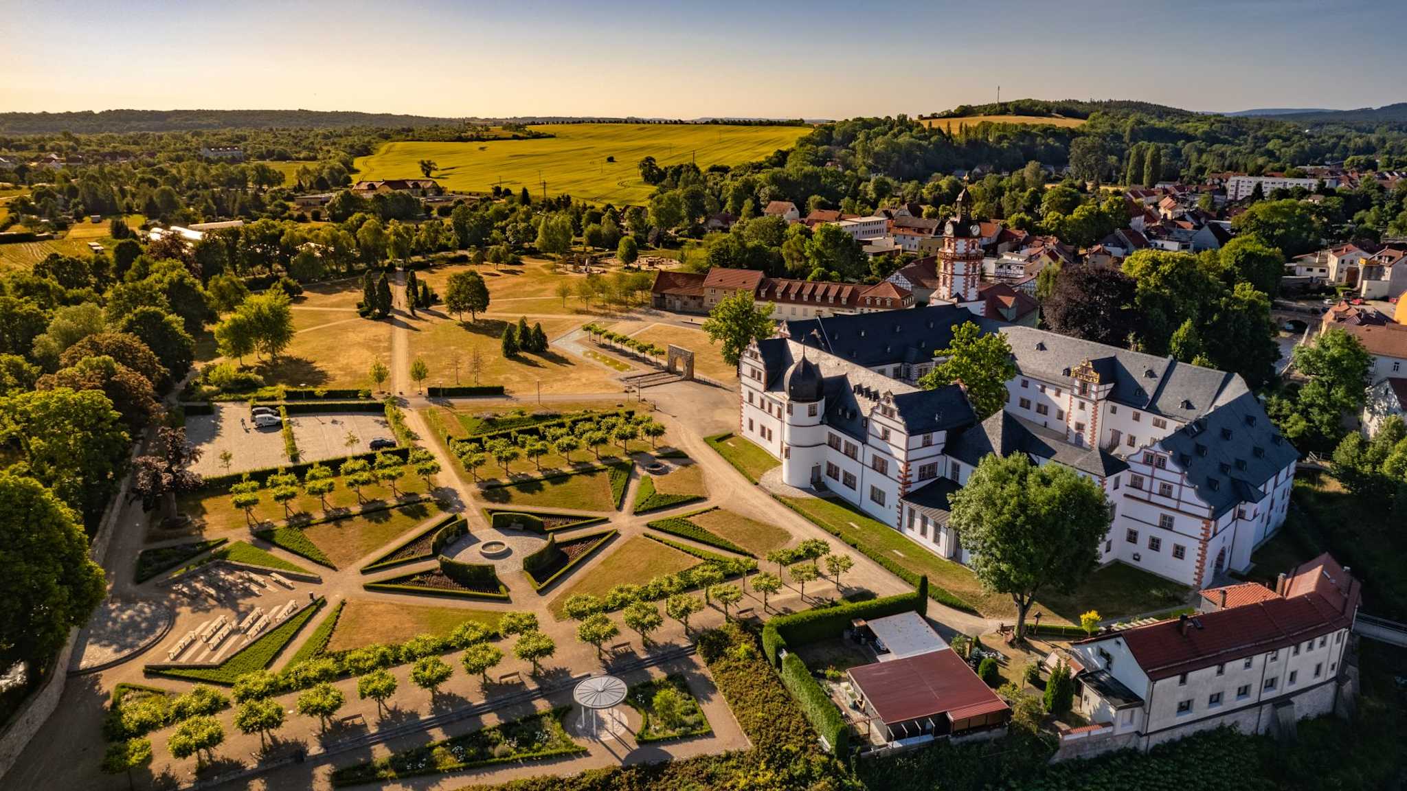 Luftperspektive auf ein Schloss am Rande einer Stadt, welches an einen großen, geometrischen Garten angrenzt.