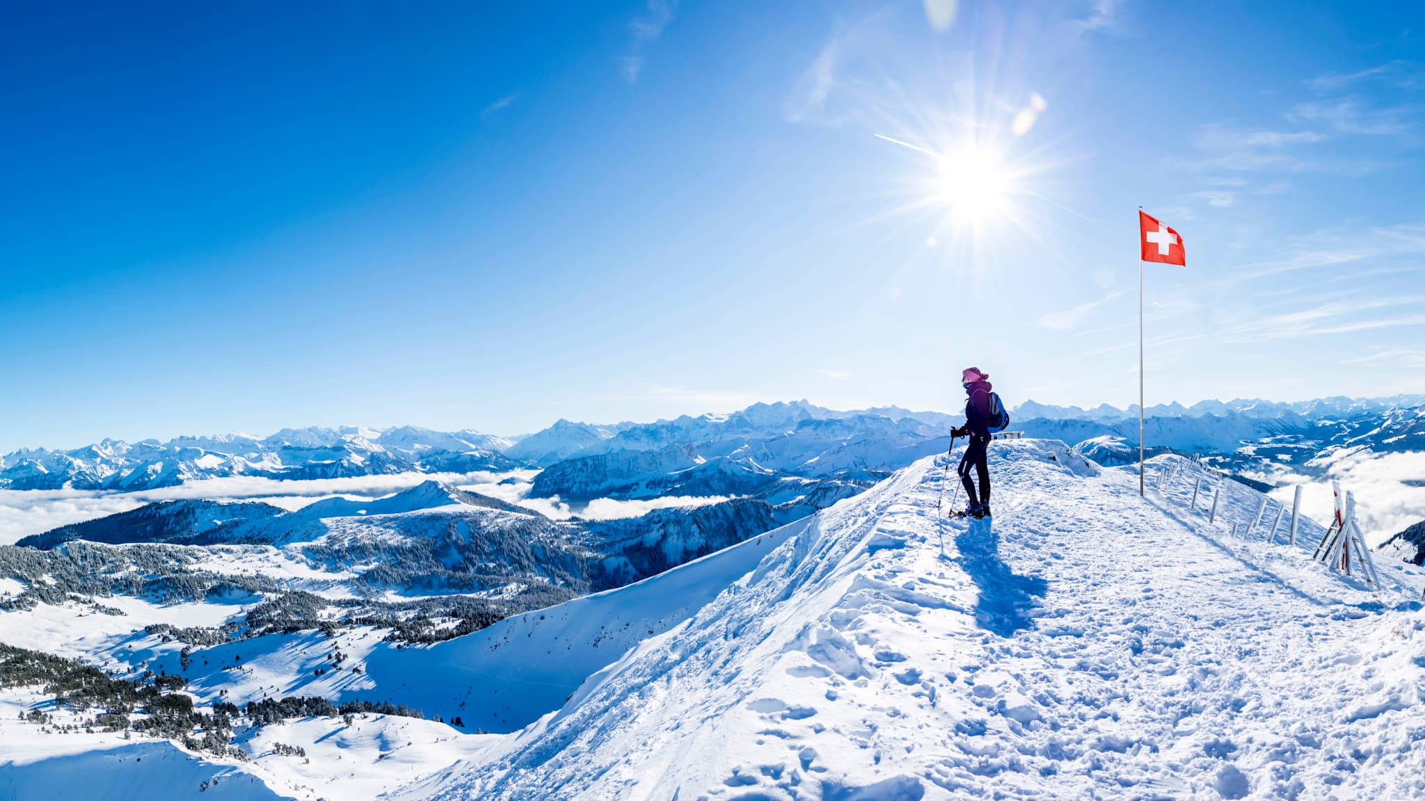 Ein Wanderer steht vor einer Schweizer Fahne auf einem Berg in den Alpen.