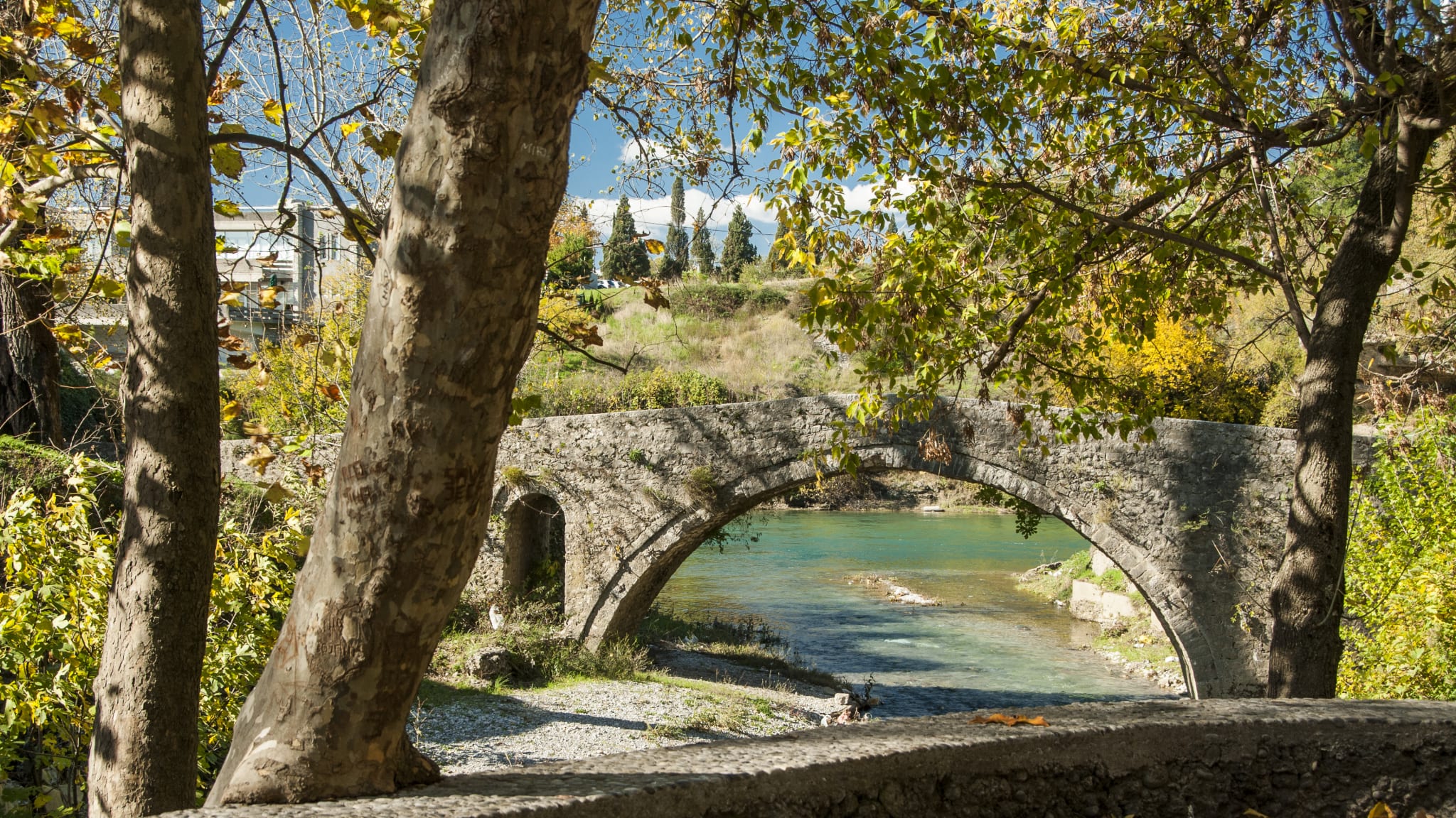 Aufnahme der Skaline, einer alten Steinbrücke. Sie kreuzt einen türkisen Fluss und ist umgeben von vielen Bäumen