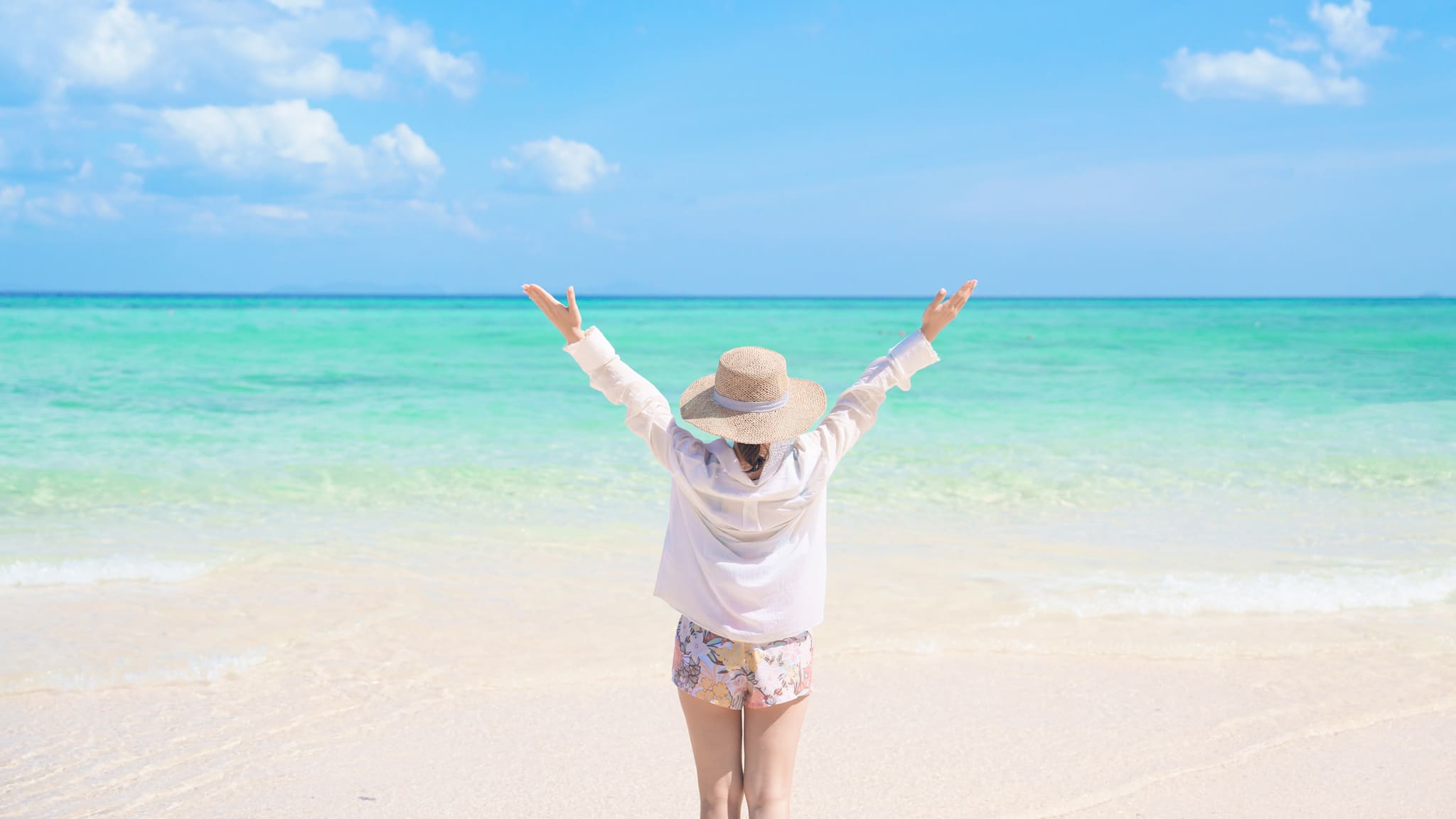 Eine Frau steht mit ausgebreiteten Armen am Meer.