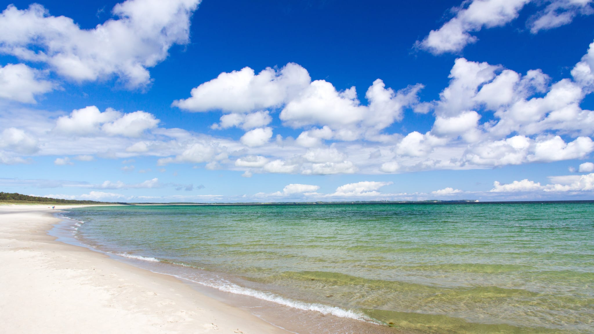 Ein langer leerer Strandabschnitt. In der Ferne spazieren zwei Menschen