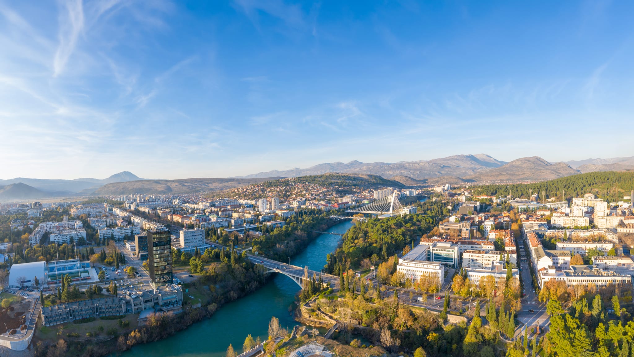 Drohnenausblick über eine Stadtkulisse. Im Hintergrund sieht man eine Bergkulisse.