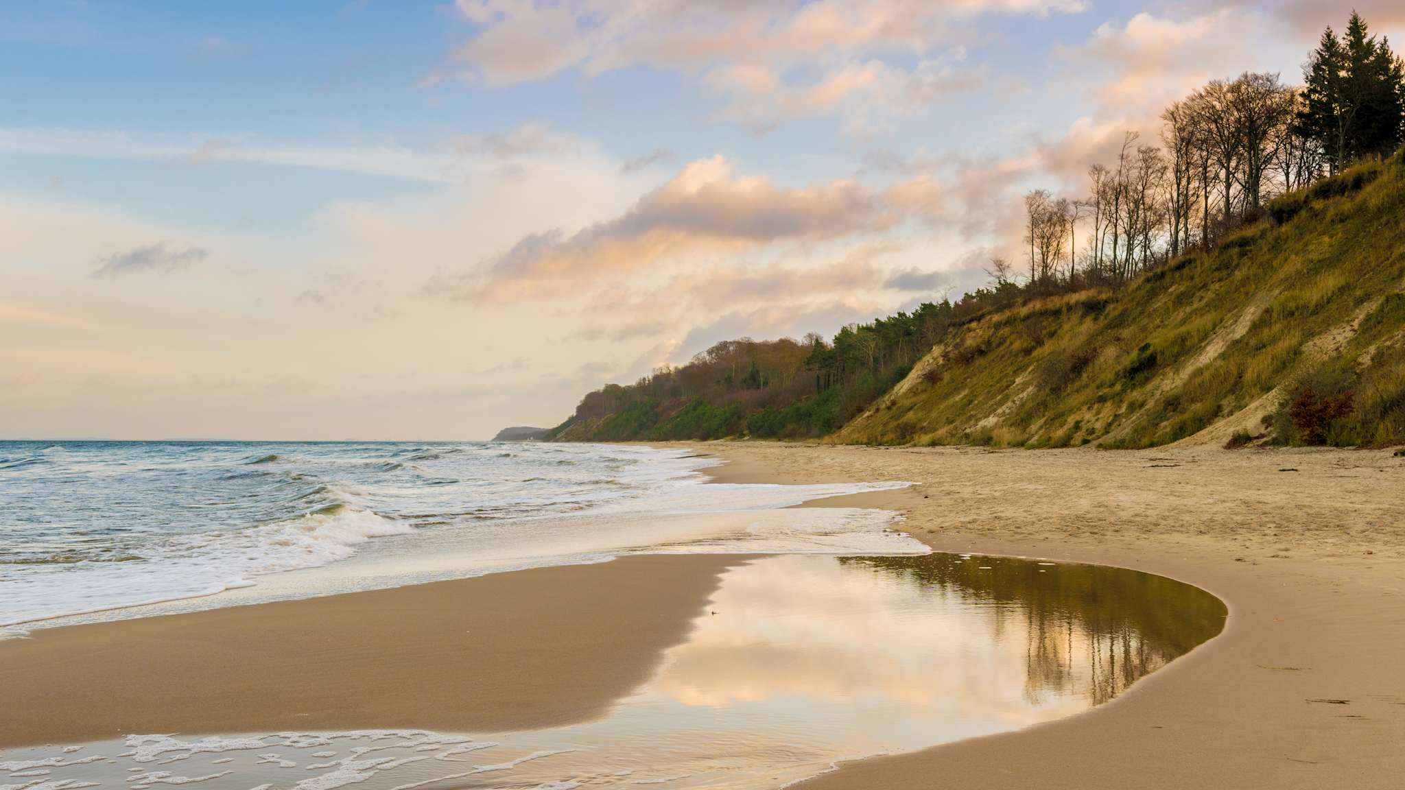 Abendstimmung an einem Strand vor einer bewaldeten Steilküste