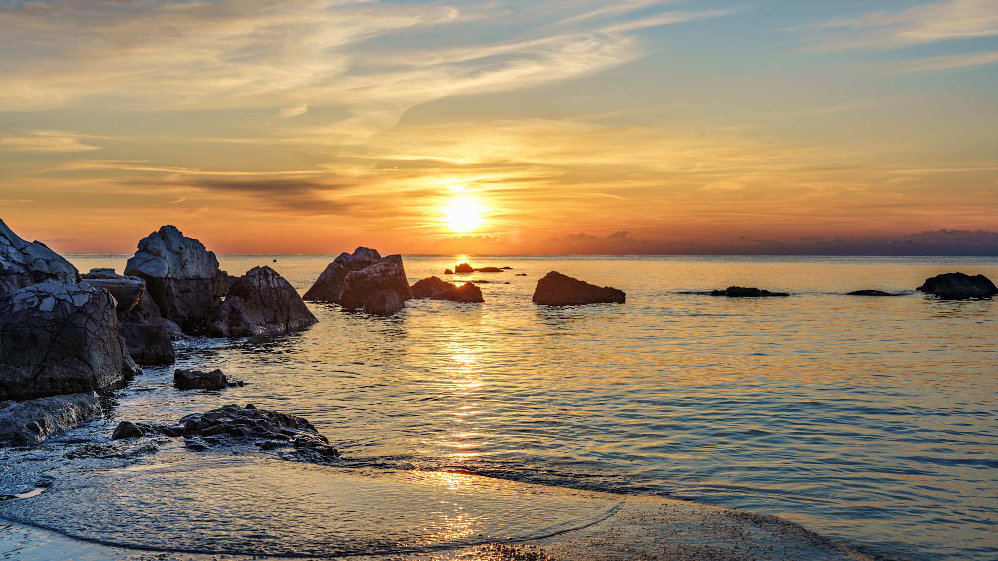 Ein Sonnenuntargang über einigen Felsen im Wasser.