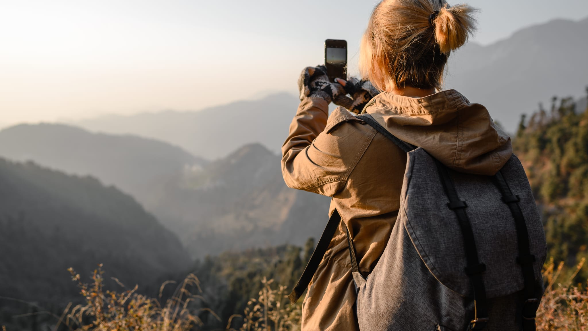 Eine Frau mit Rucksack macht ein Foto von einer Landschaft mit dem Smartphone